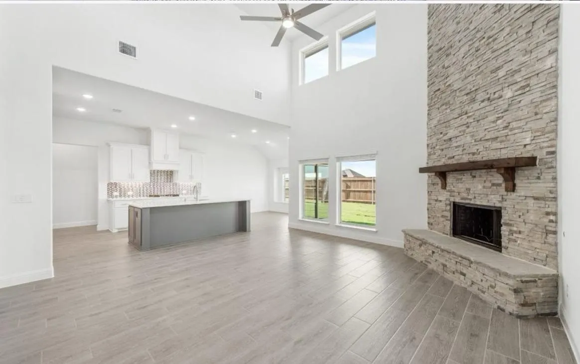 Unfurnished living room featuring a stone fireplace, light wood-type flooring, ceiling fan, and a towering ceiling