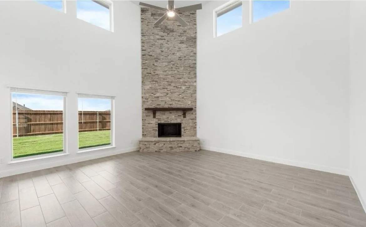 Unfurnished living room with a high ceiling, wood finished floors, a ceiling fan, and a stone fireplace