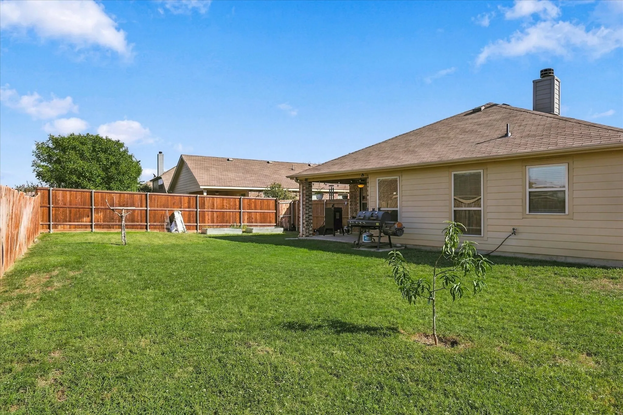 Expansive grassy yard with wood fencing, a covered patio, and a light-colored exterior with multiple windows