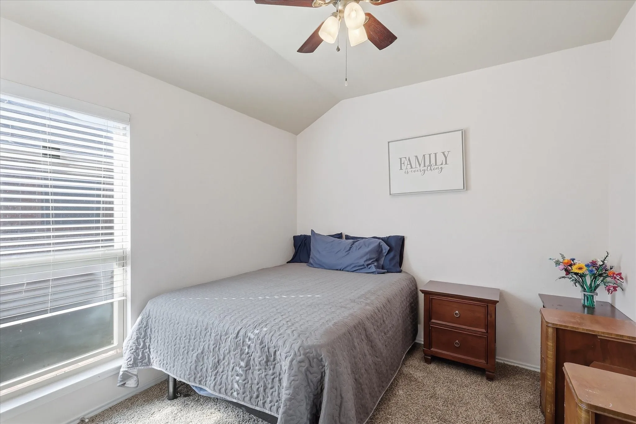 Room featuring a vaulted ceiling with a ceiling fan, a window with horizontal blinds, and carpeted flooring