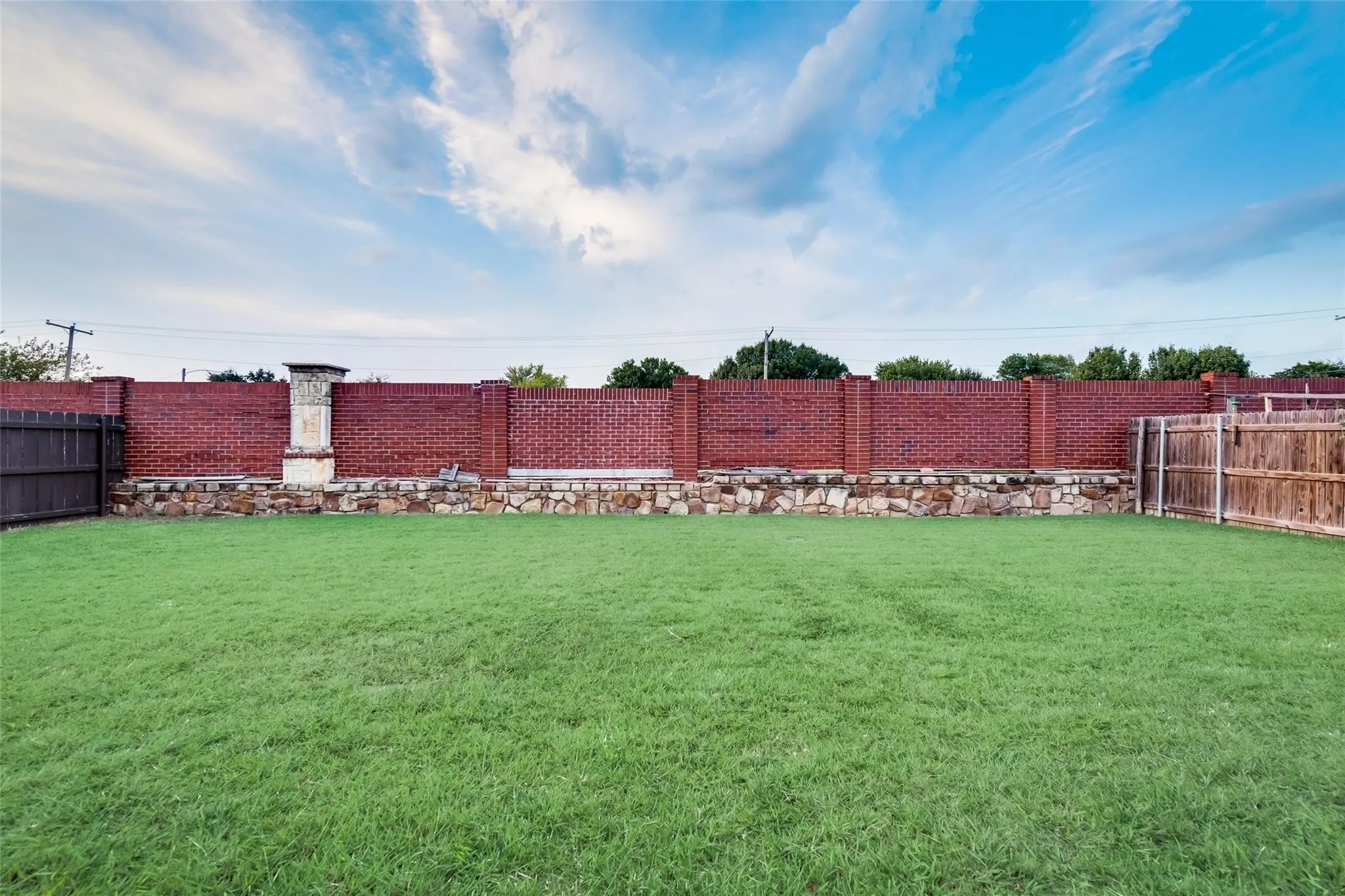 Expansive lawn area with a perimeter brick wall, stone retaining wall, and wood fencing