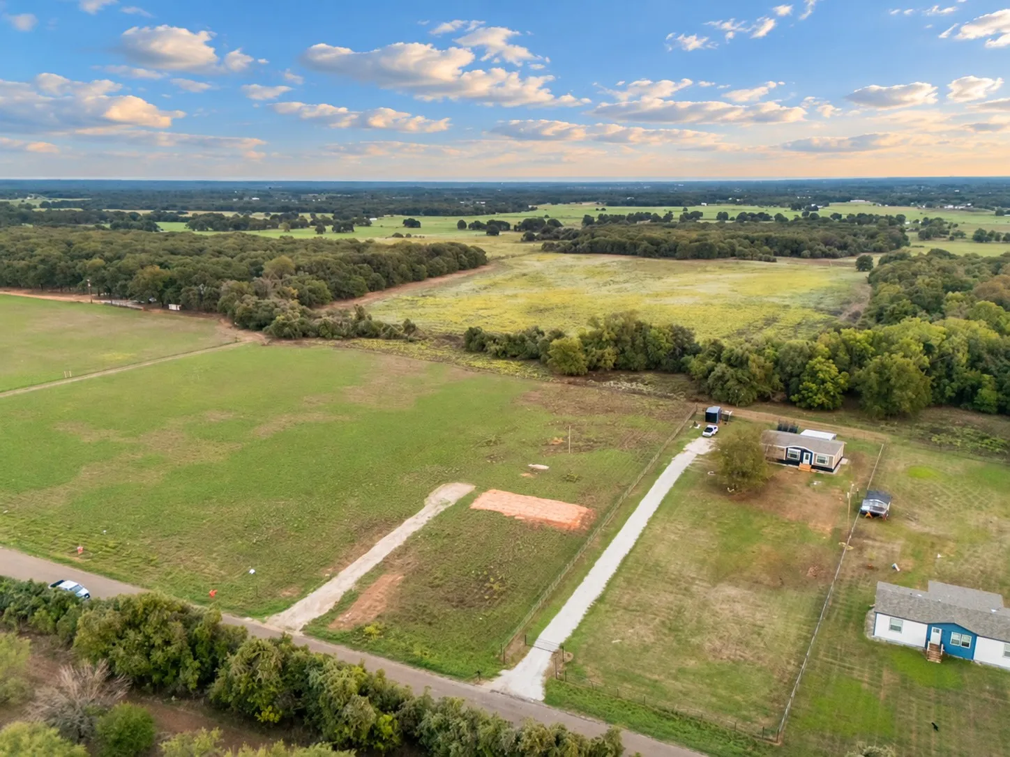 Expansive acreage featuring a gravel drive, established fencing, and surrounding mature trees
