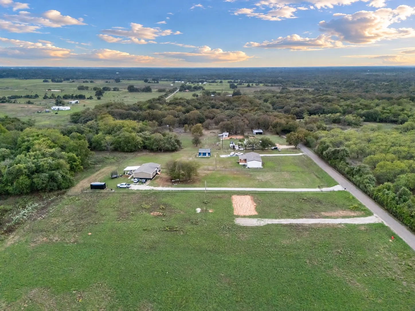 Expansive acreage featuring multiple structures, mature trees, and a paved road frontage