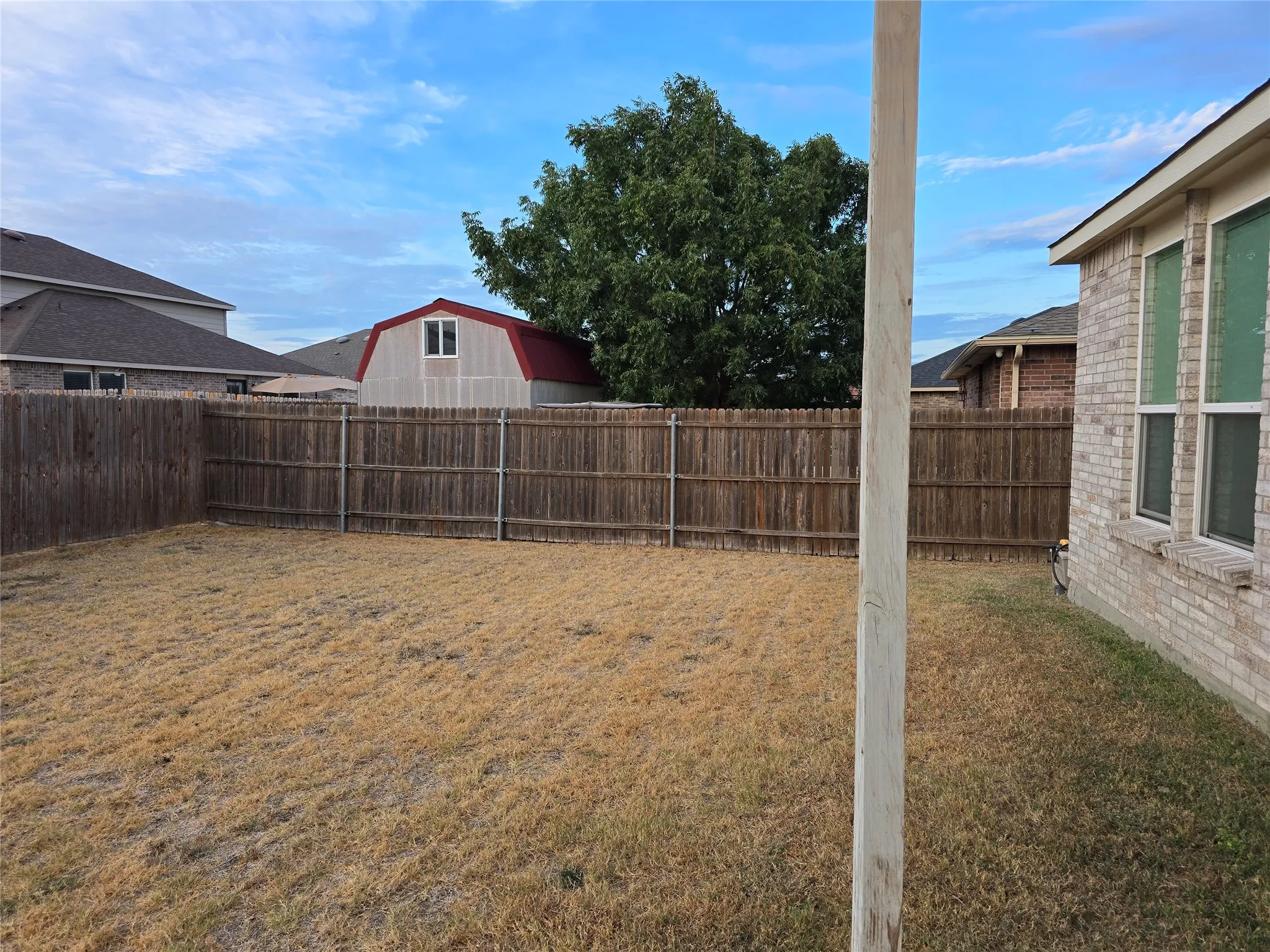 Fenced backyard featuring a wood privacy fence, a brick exterior wall, and multiple windows