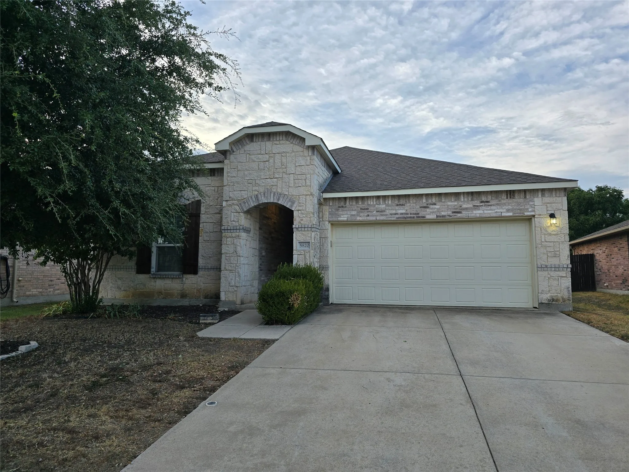 Stone façade with brick accents, arched entryway, attached garage with panel door, and concrete driveway