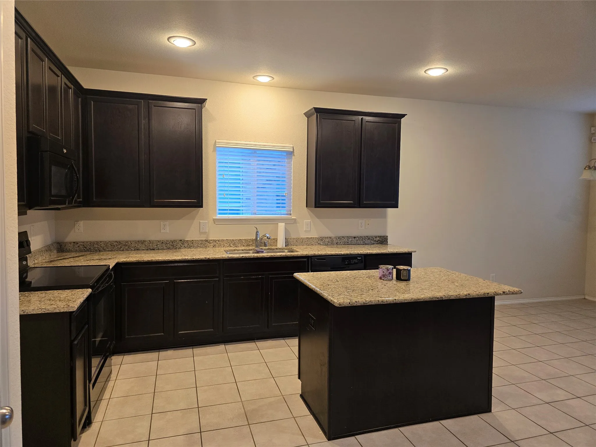 Dark wood-finish cabinetry, light-colored speckled countertops, stainless steel sink with gooseneck faucet, black built-in appliances, and a central island