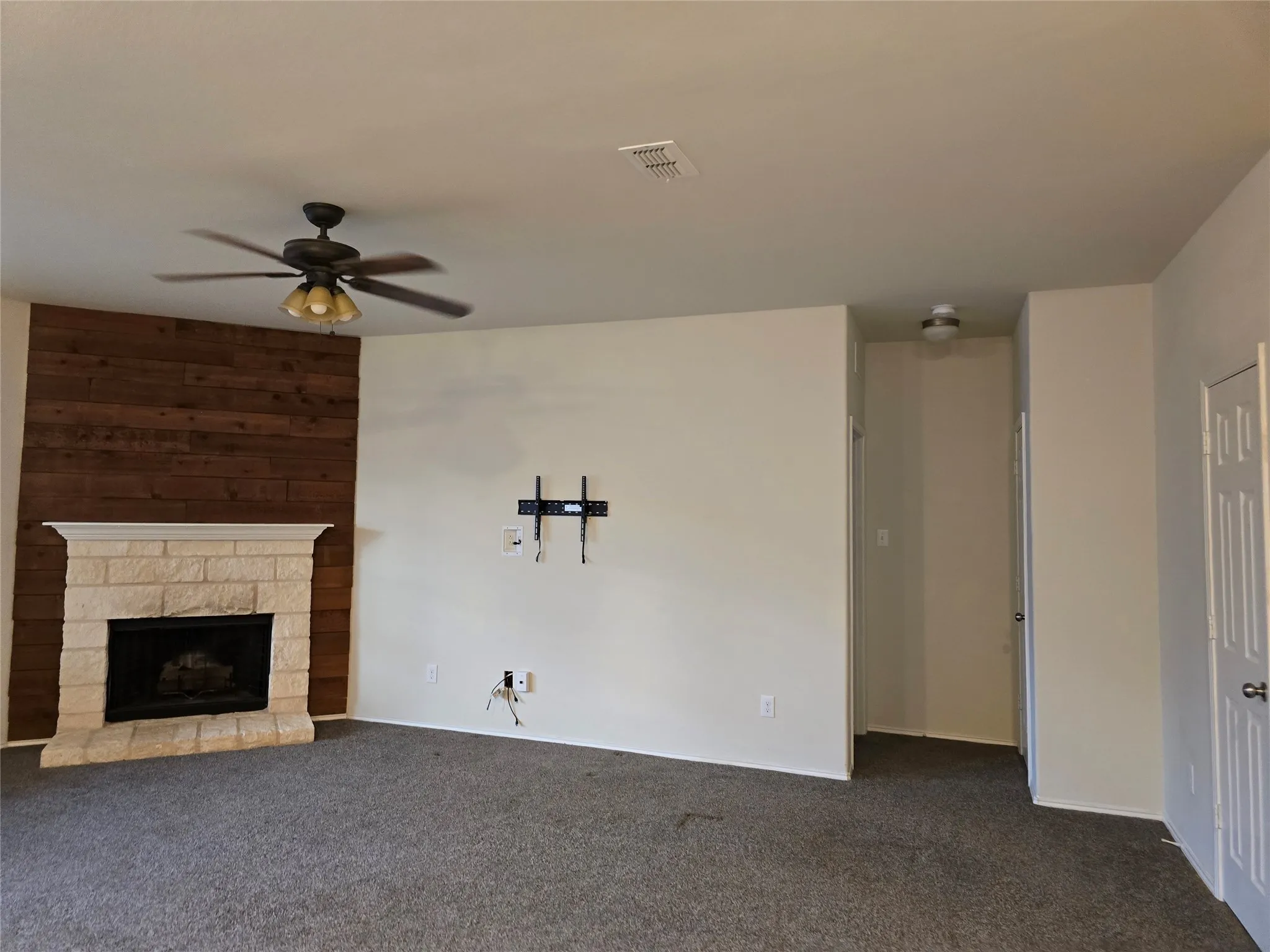 Fireplace featuring a stone surround and wood-paneled accent wall, ceiling fan with integrated lighting, and carpet flooring