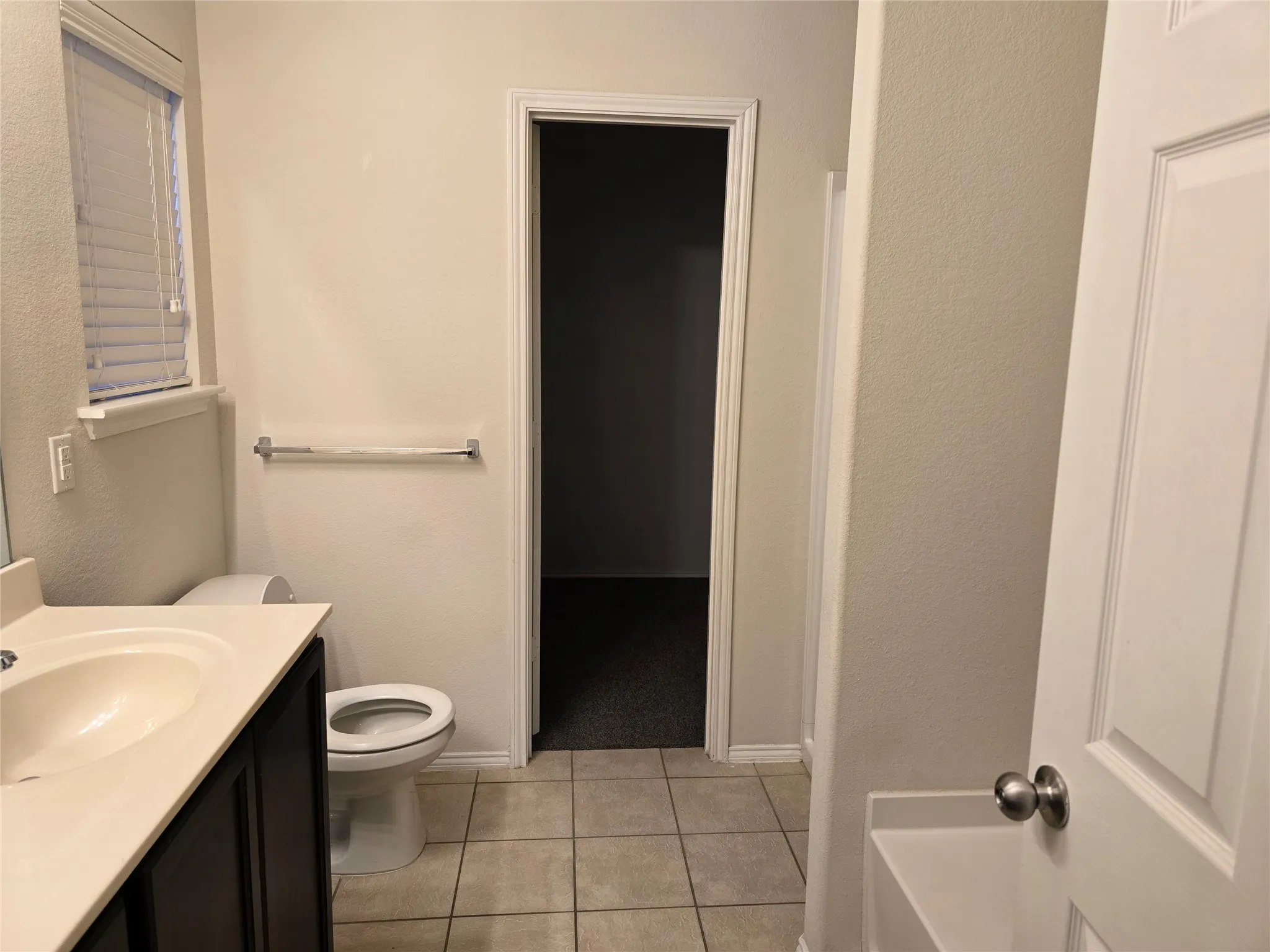 Tile flooring, dark wood-finish vanity, light-toned countertop, and window with blinds