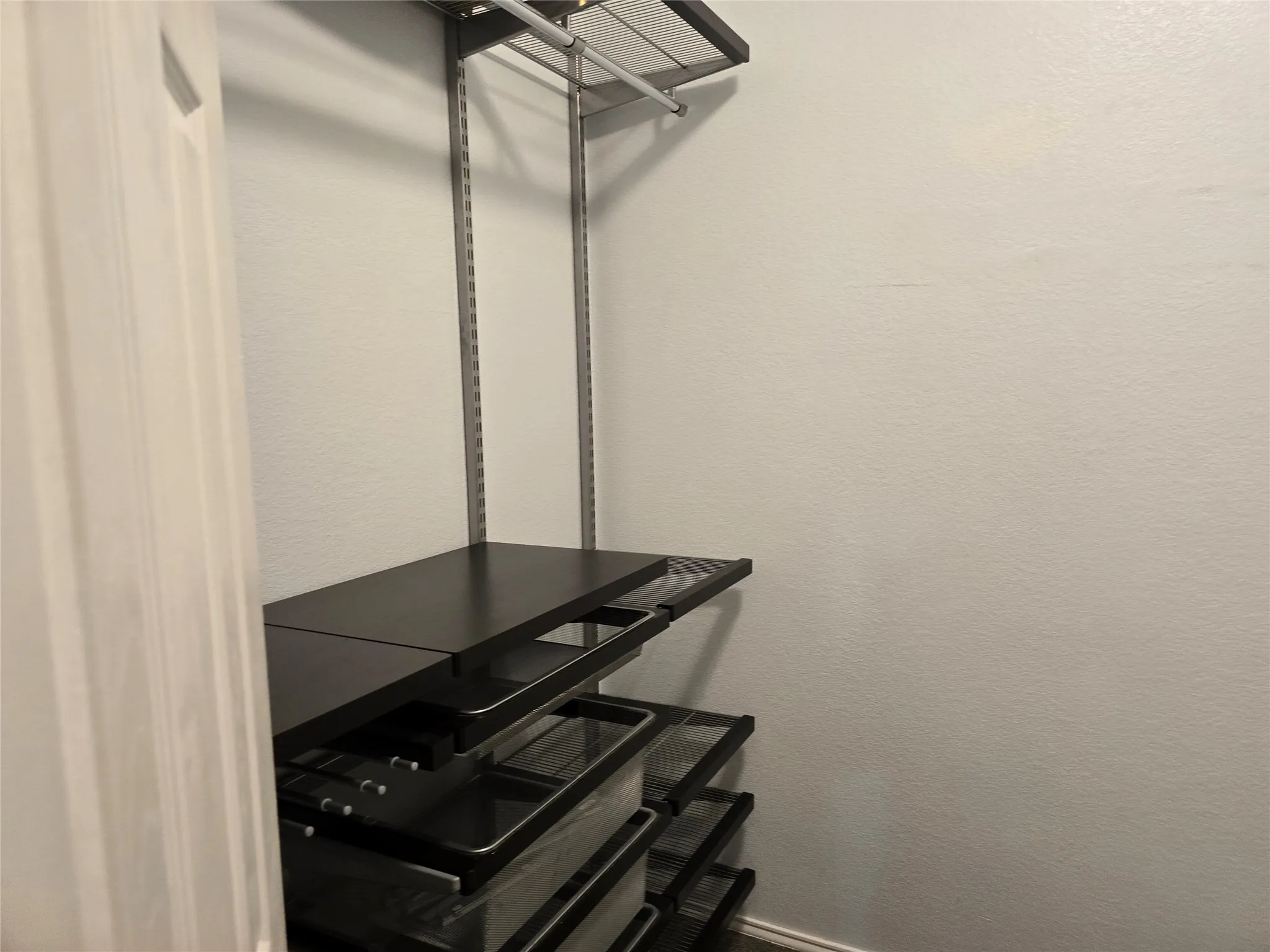 Built-in closet organization system featuring dark wood-finish shelving, metal hanging rods, and pull-out drawers