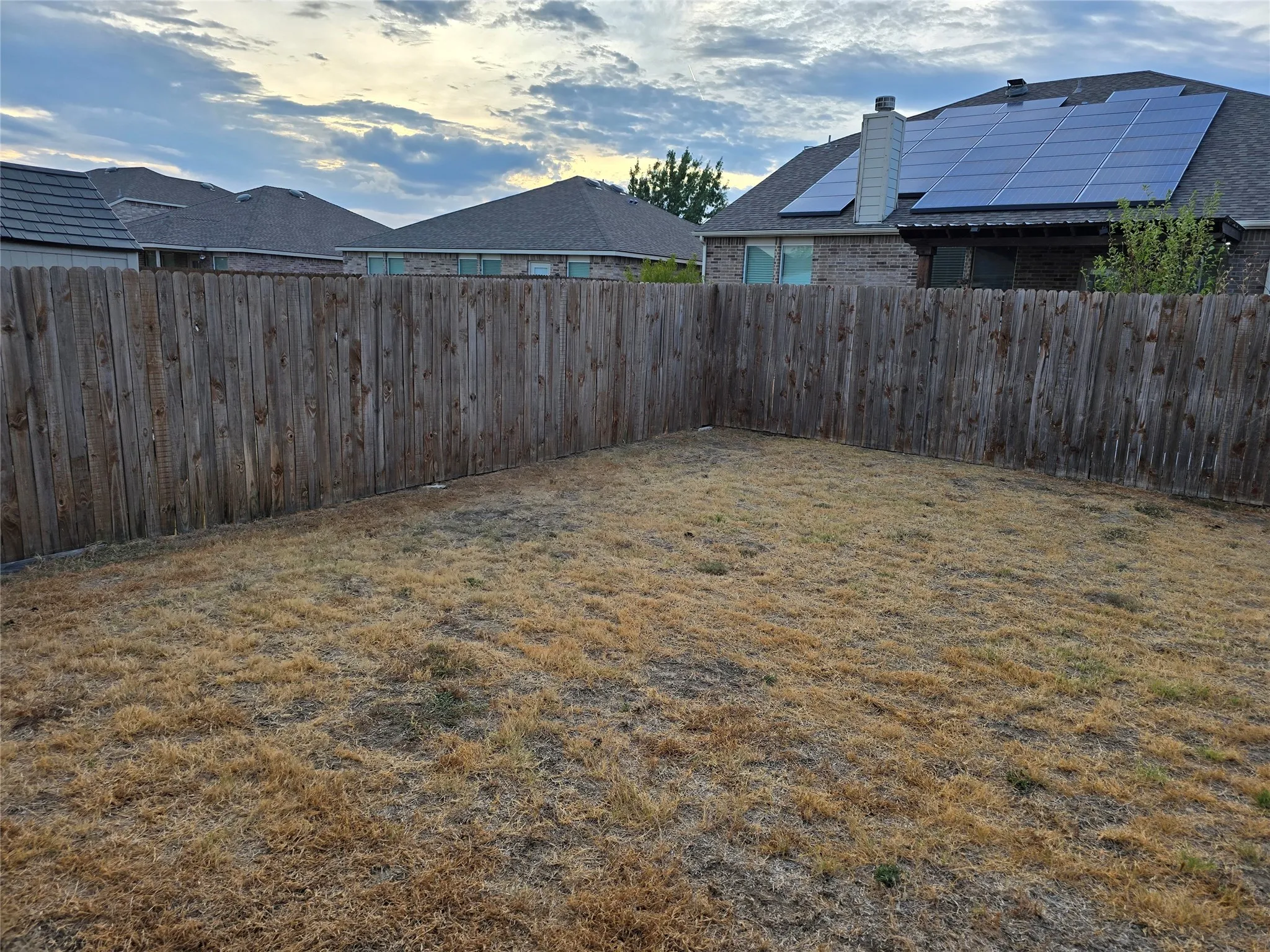 Fenced backyard featuring a wood fence perimeter and a partially visible residential structure with solar panels