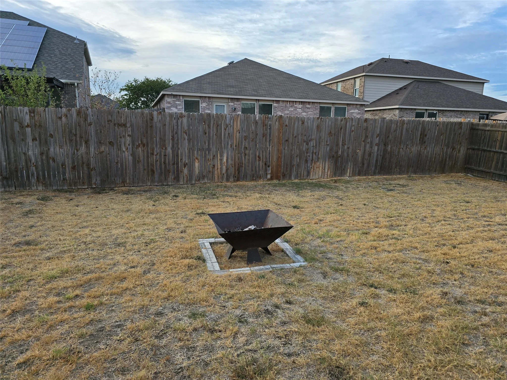 Expansive backyard featuring a wood privacy fence and a built-in fire pit with a paver surround