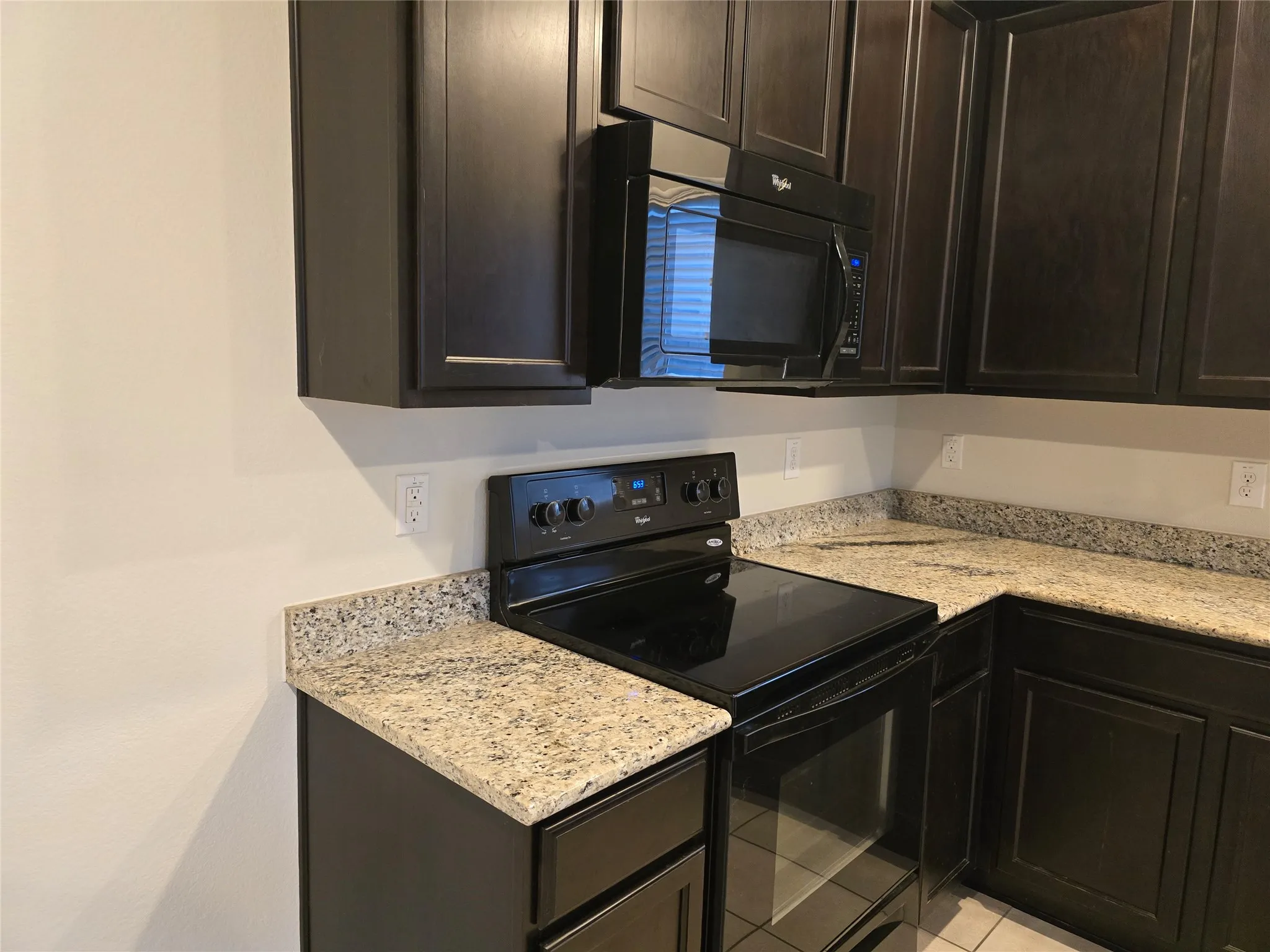 Dark wood-finish cabinetry, light-toned speckled countertops, and integrated black appliances