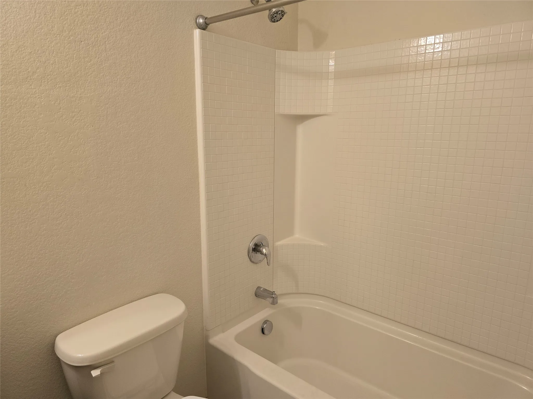 White shower/tub combination with chrome fixtures and integrated shelving