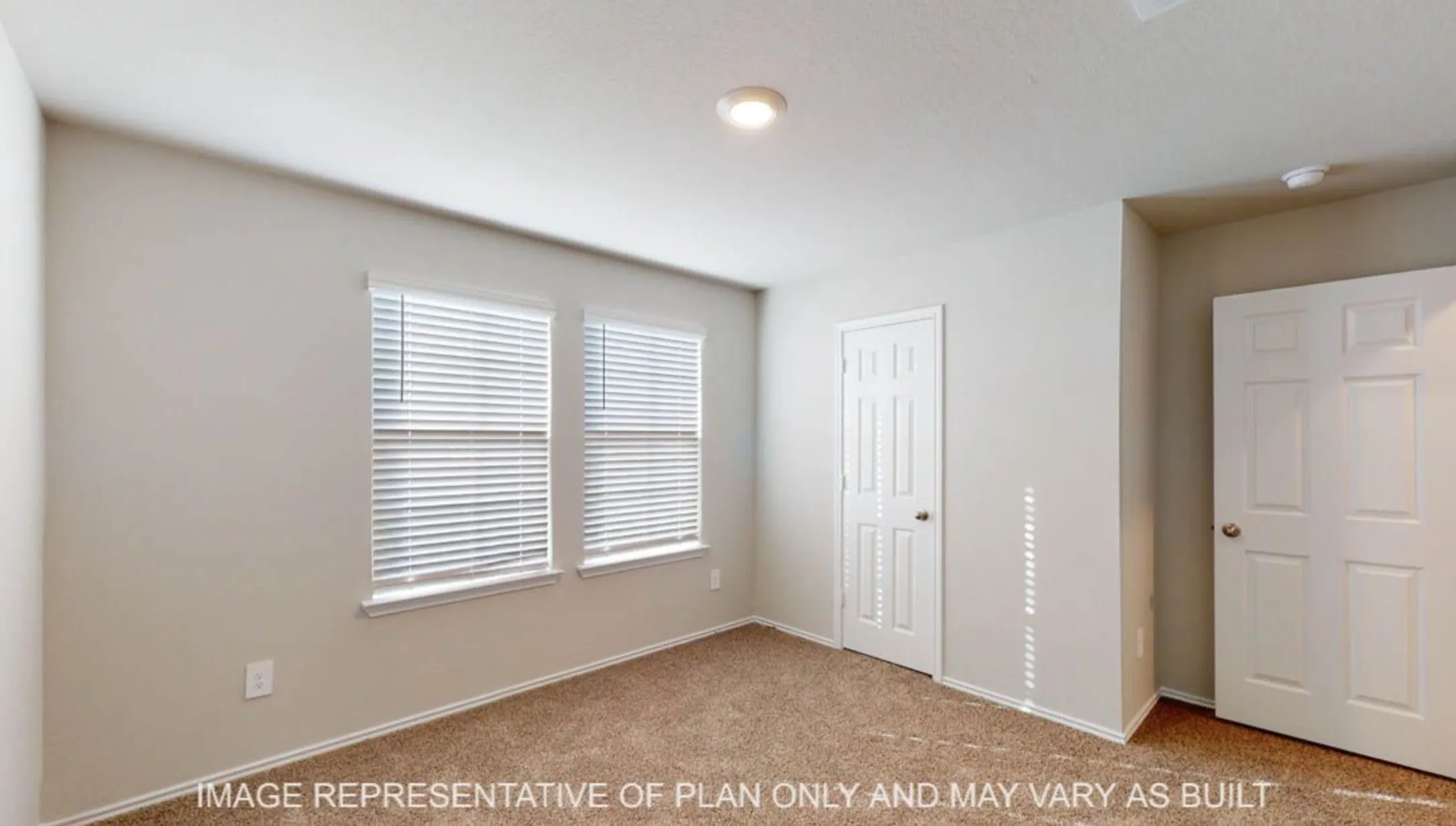 Wall-to-wall carpeting in a neutral tone, two windows with blinds, a recessed ceiling light, and two paneled doors with hardware