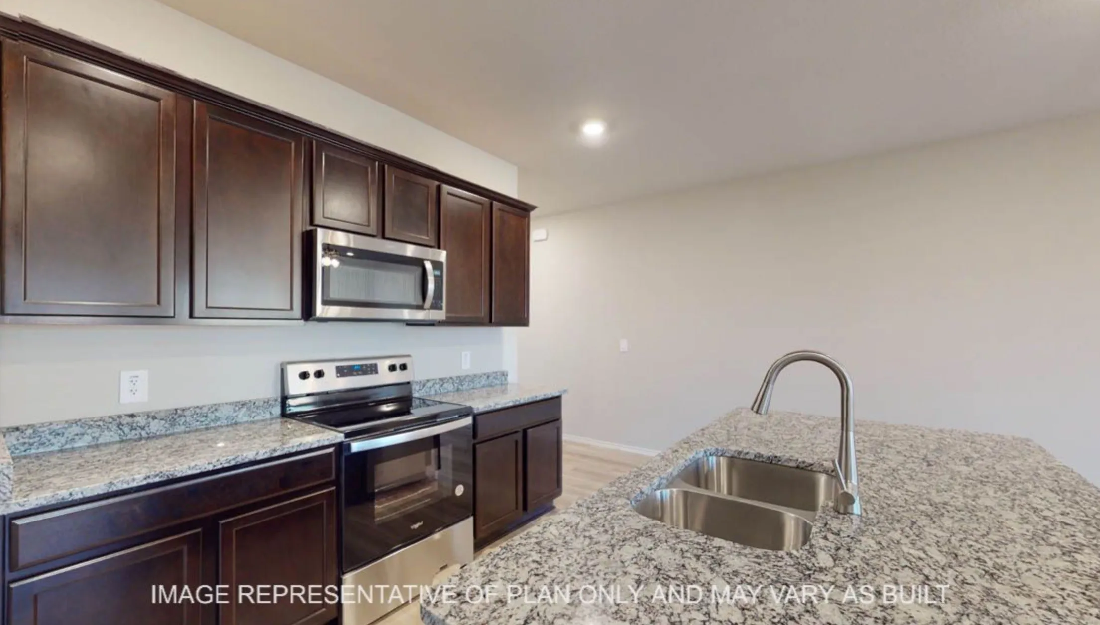 Dark wood-finish cabinetry, stainless steel appliances, speckled stone countertops, and an undermount double basin sink with a high-arc faucet