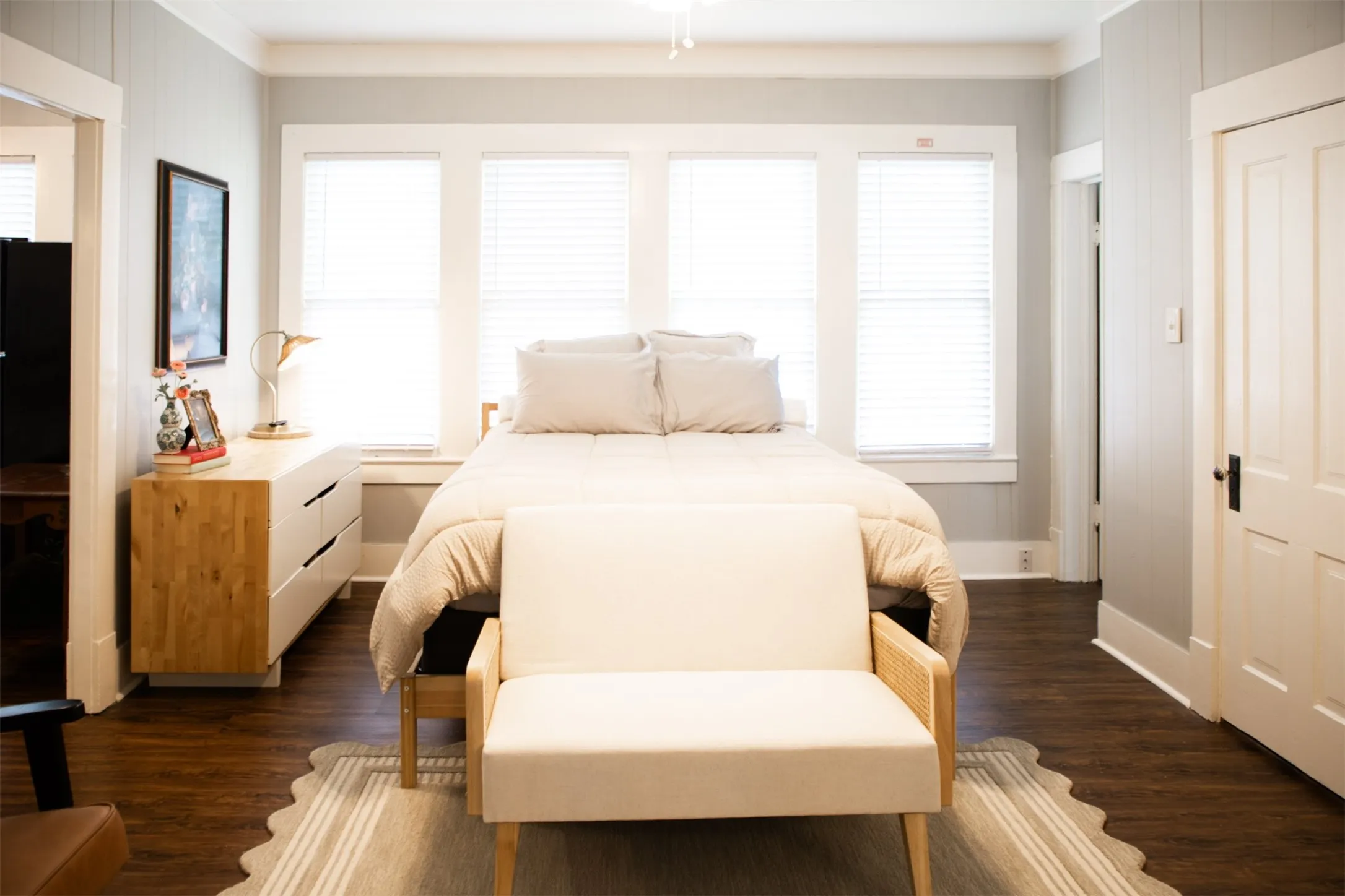 Three large windows with blinds, dark wood-finish flooring, white trim, and a paneled door with black hardware