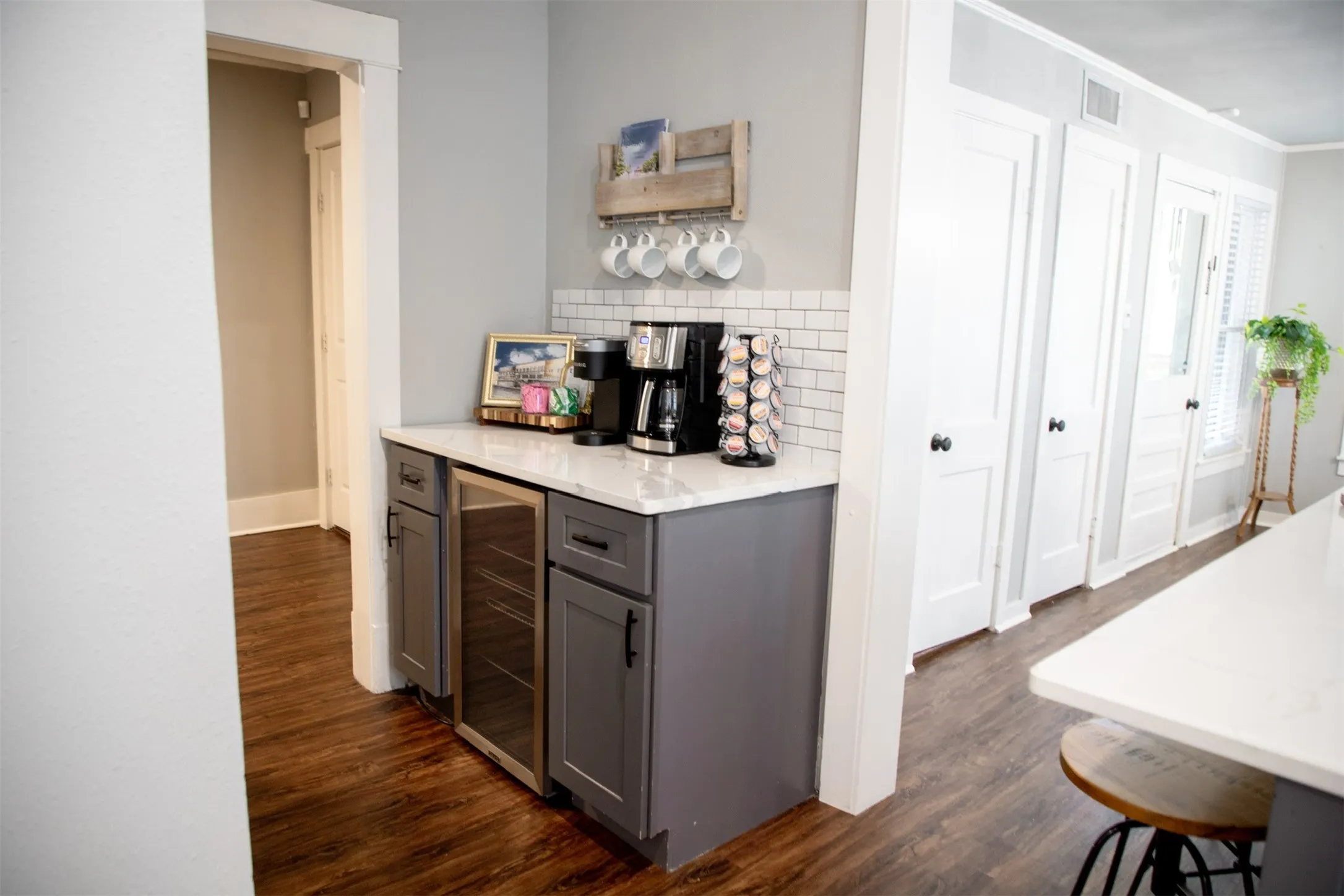 Built-in beverage cooler, white subway tile backsplash, dark wood-finish flooring, white countertop, and gray cabinetry
