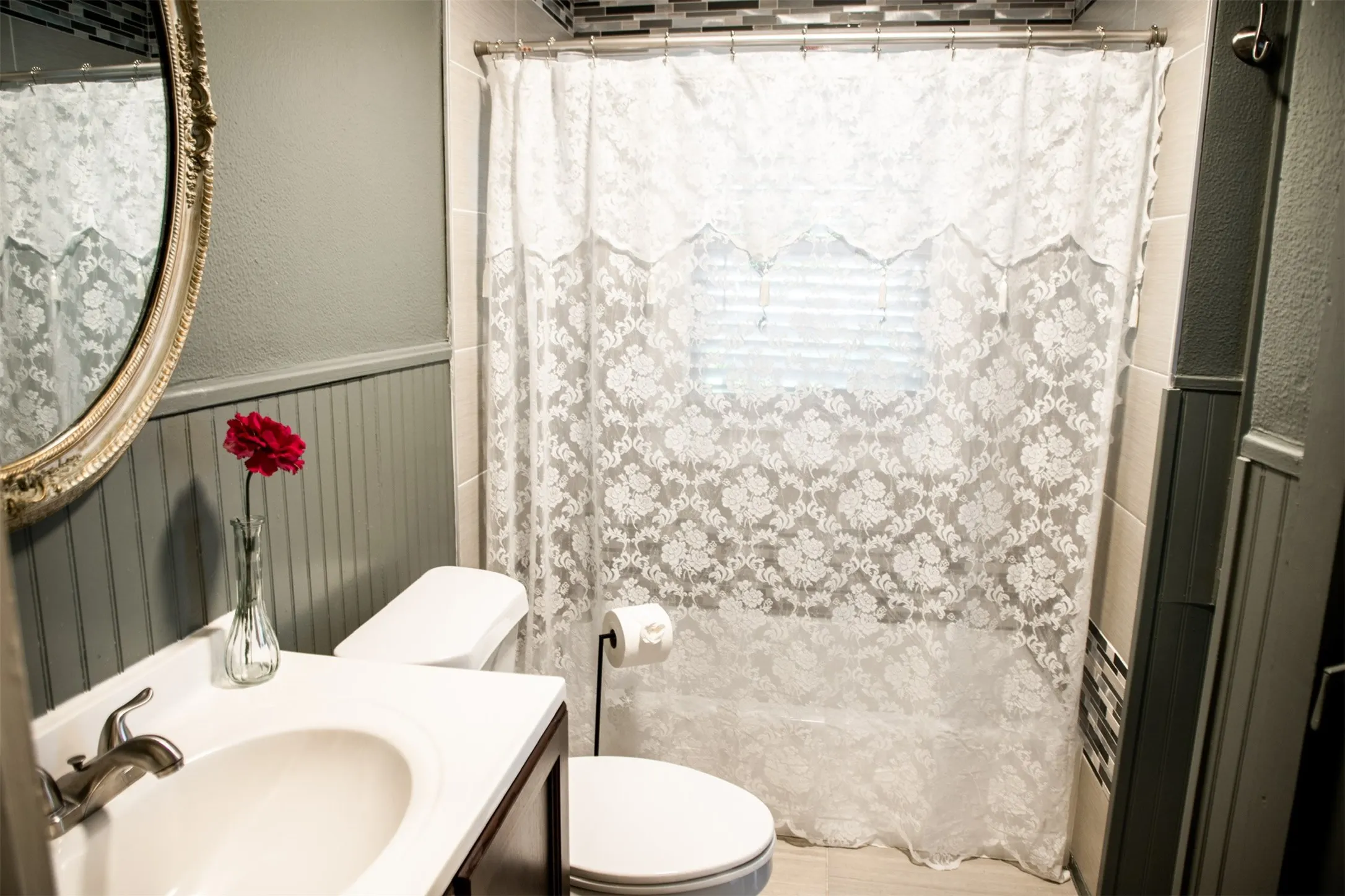 Vanity with integrated sink, beadboard wainscoting, decorative wall mirror, and tiled shower surround