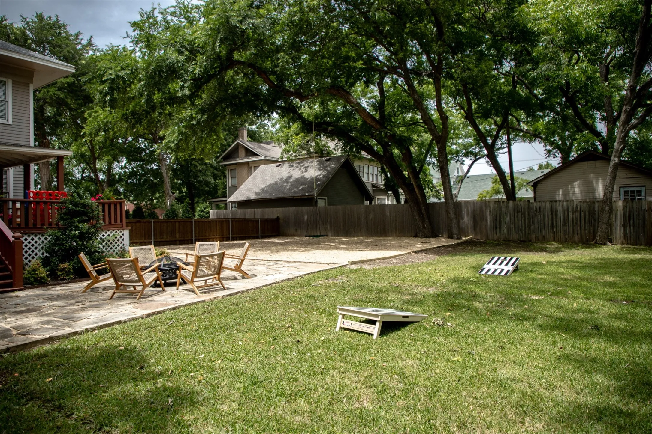 Expansive rear yard featuring a natural stone patio, a dedicated gravel area, a surrounding wood privacy fence, and mature trees providing canopy