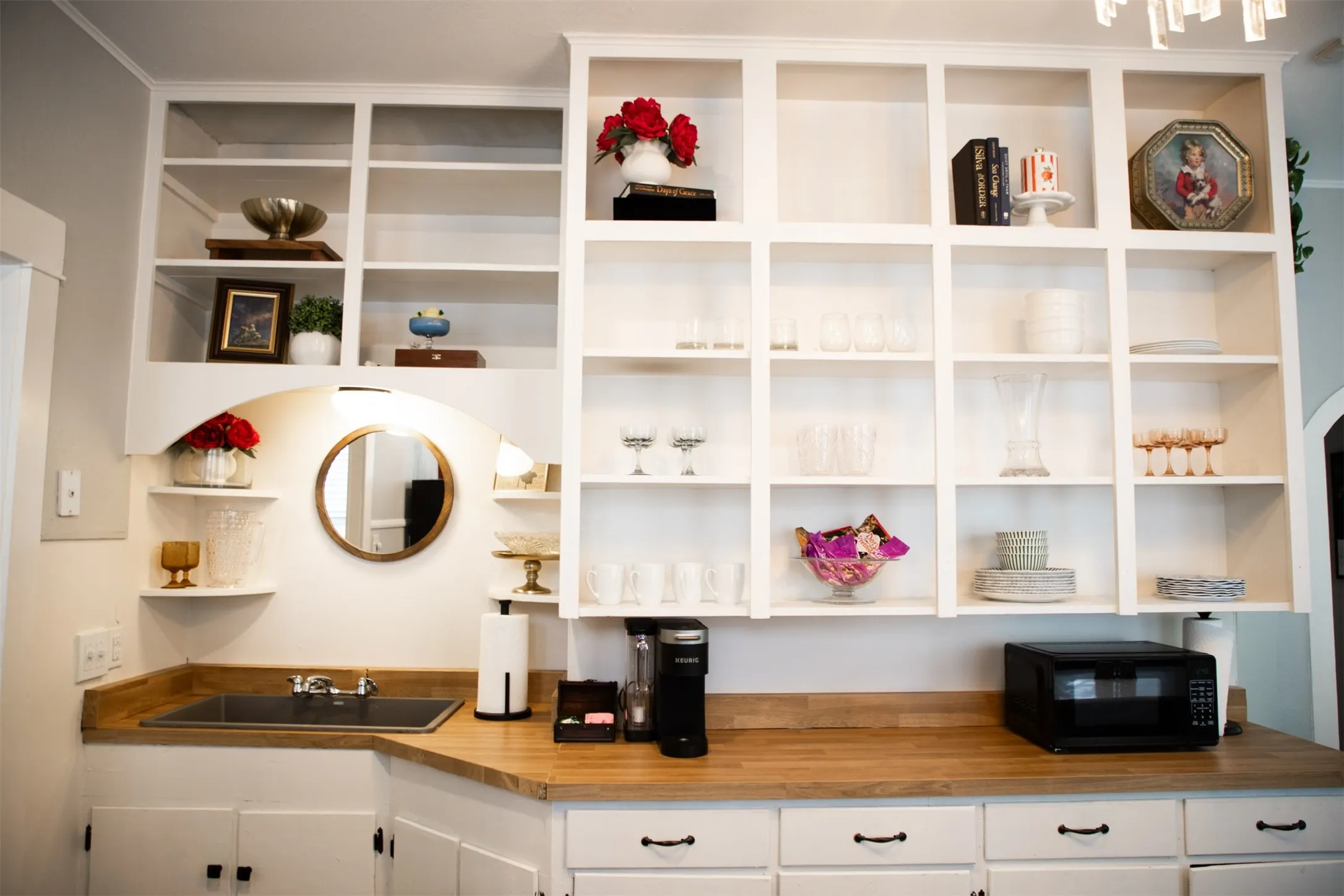 White built-in shelving, wood-finish countertops, undermount sink, and lower cabinetry with black hardware