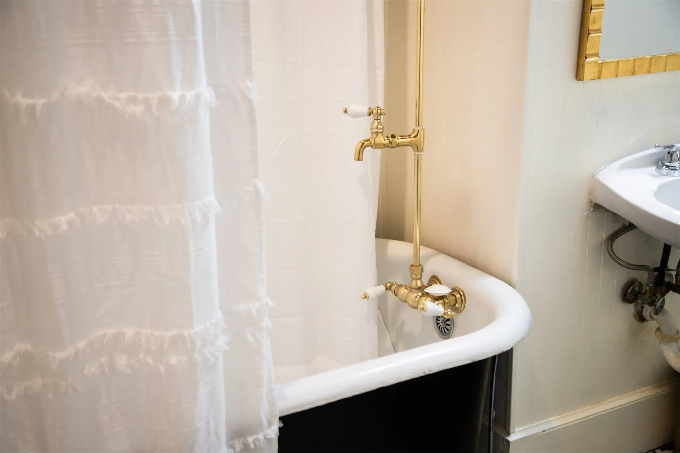 Clawfoot tub with brass fixtures and a wall-mounted sink