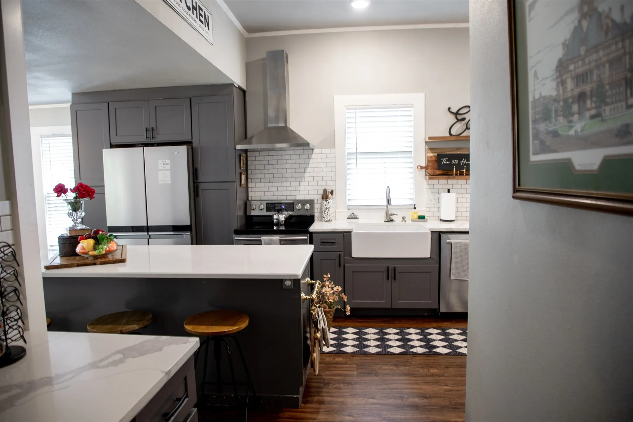 Kitchen featuring a large island with a light-toned countertop, dark wood-finish flooring, white subway tile backsplash, and a white farmhouse-style sink