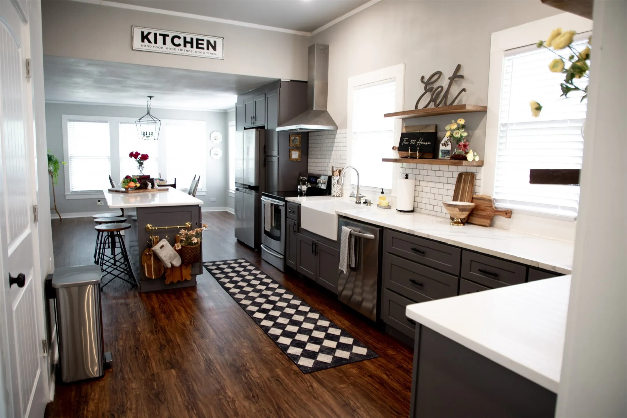 Wood-finish flooring, white countertops, subway tile backsplash, dark-finish cabinetry, and a farmhouse sink