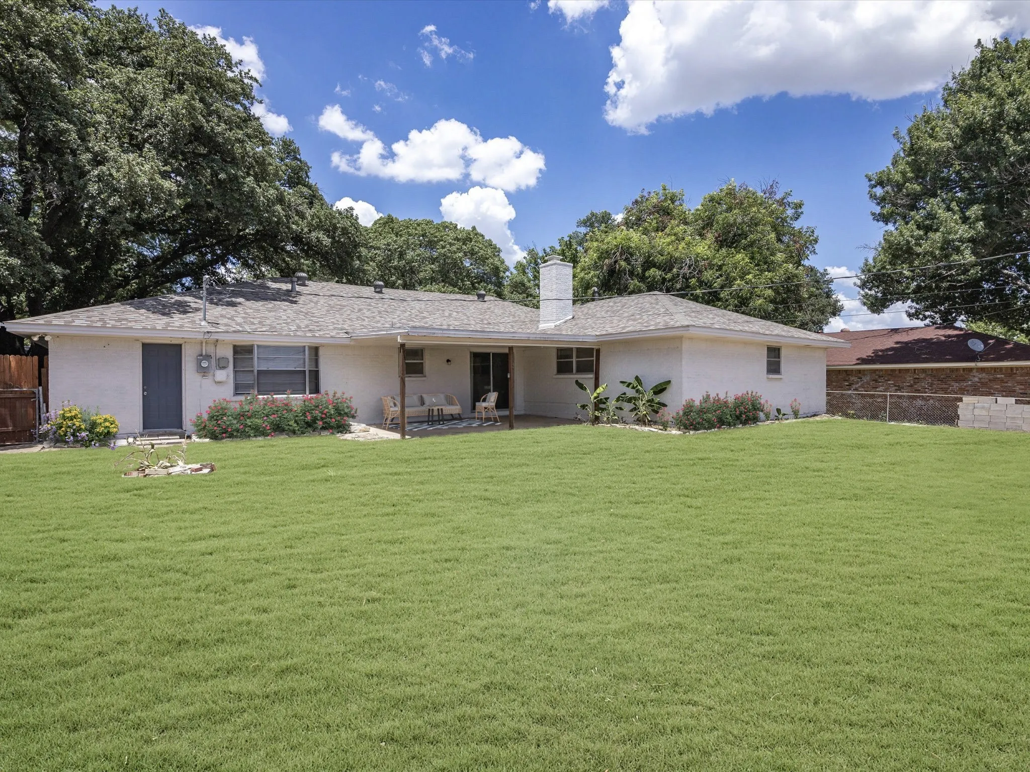 Expansive green lawn, covered patio, white stucco exterior, established perimeter trees, and a privacy fence