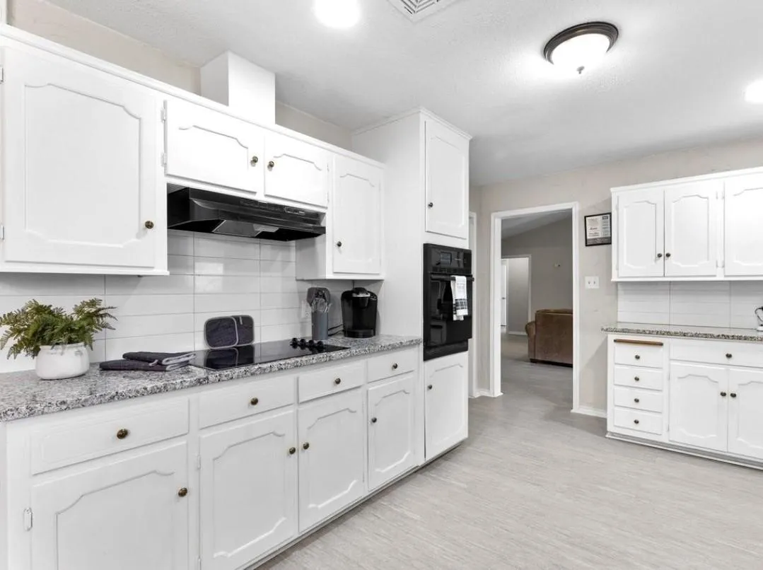 Kitchen featuring white cabinetry, granite countertops, tile backsplash, built-in oven, and light-tone flooring
