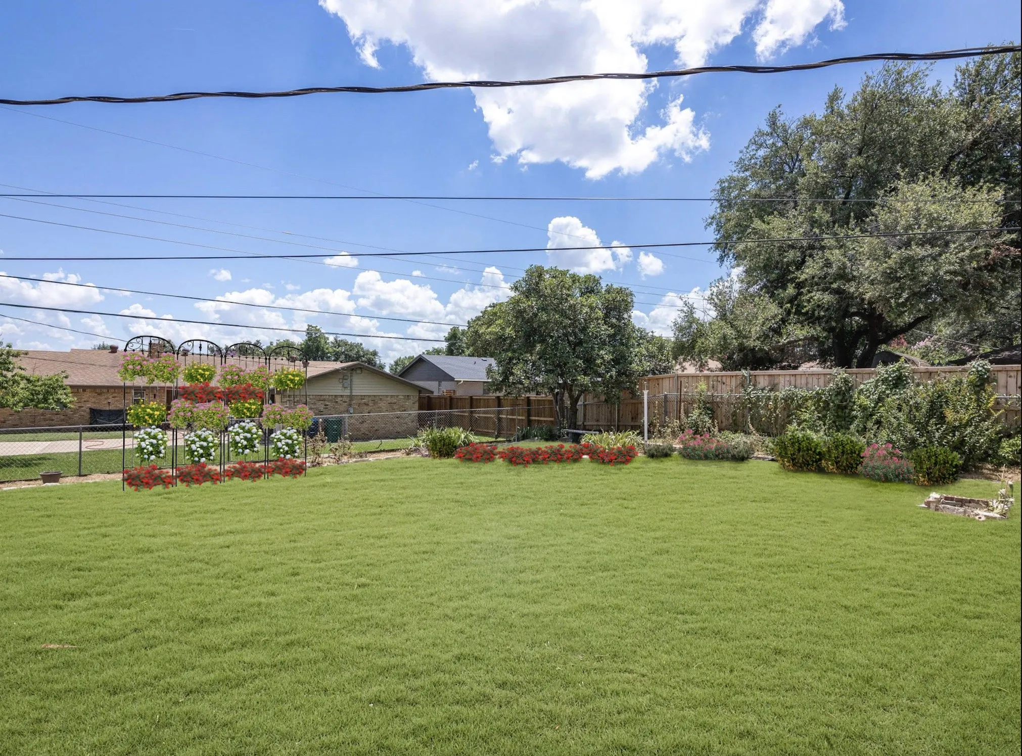 Expansive green lawn with mature perimeter trees, a wood privacy fence, and planted flower beds