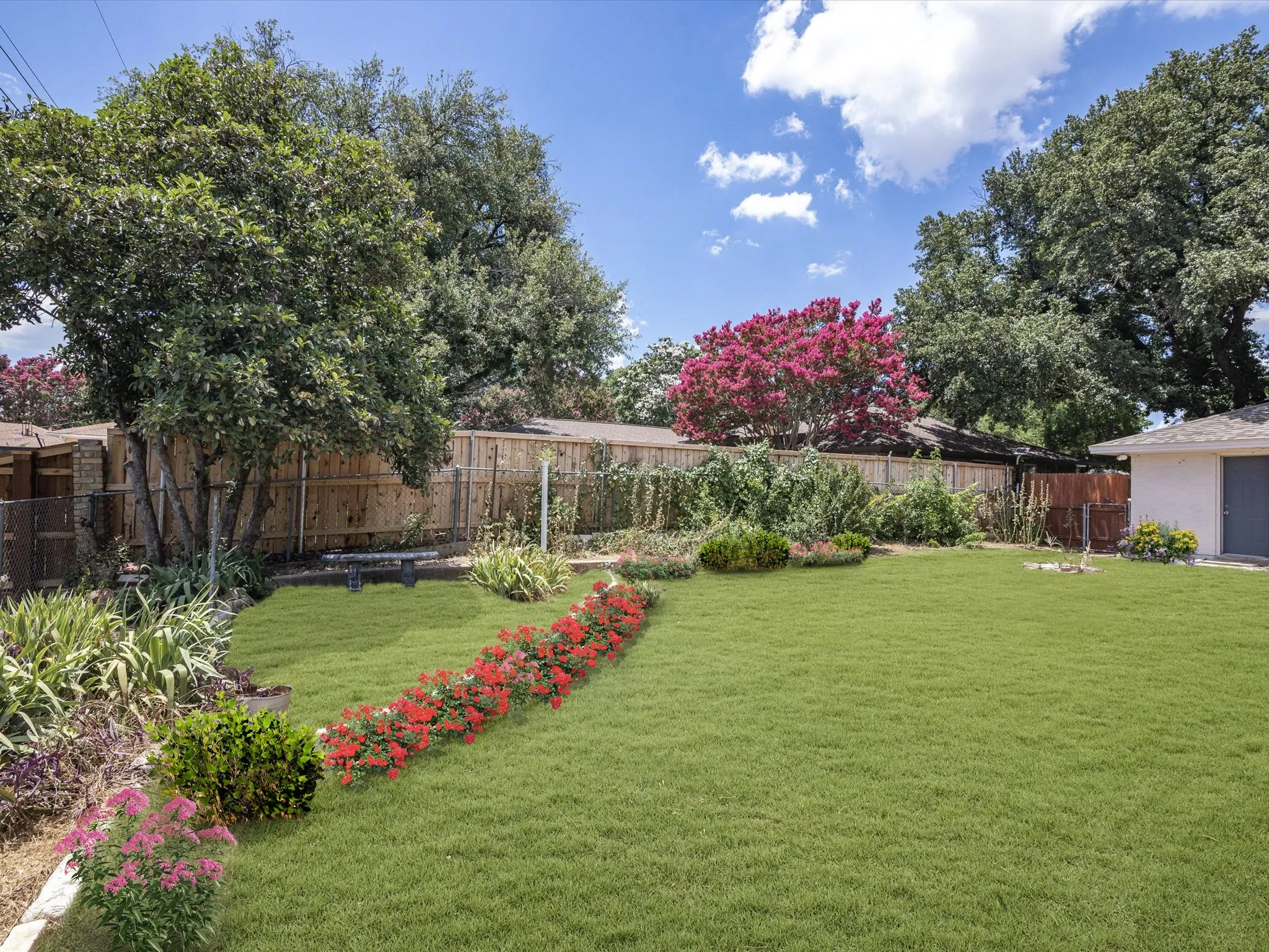 Expansive lawn area with a decorative stone bench, various plantings, and a wooden privacy fence