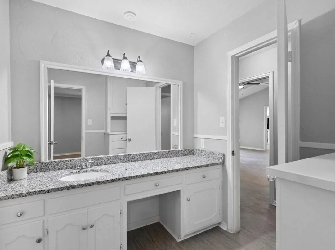 Spacious vanity with an integrated sink, granite countertop, white cabinetry, and wood-finish flooring