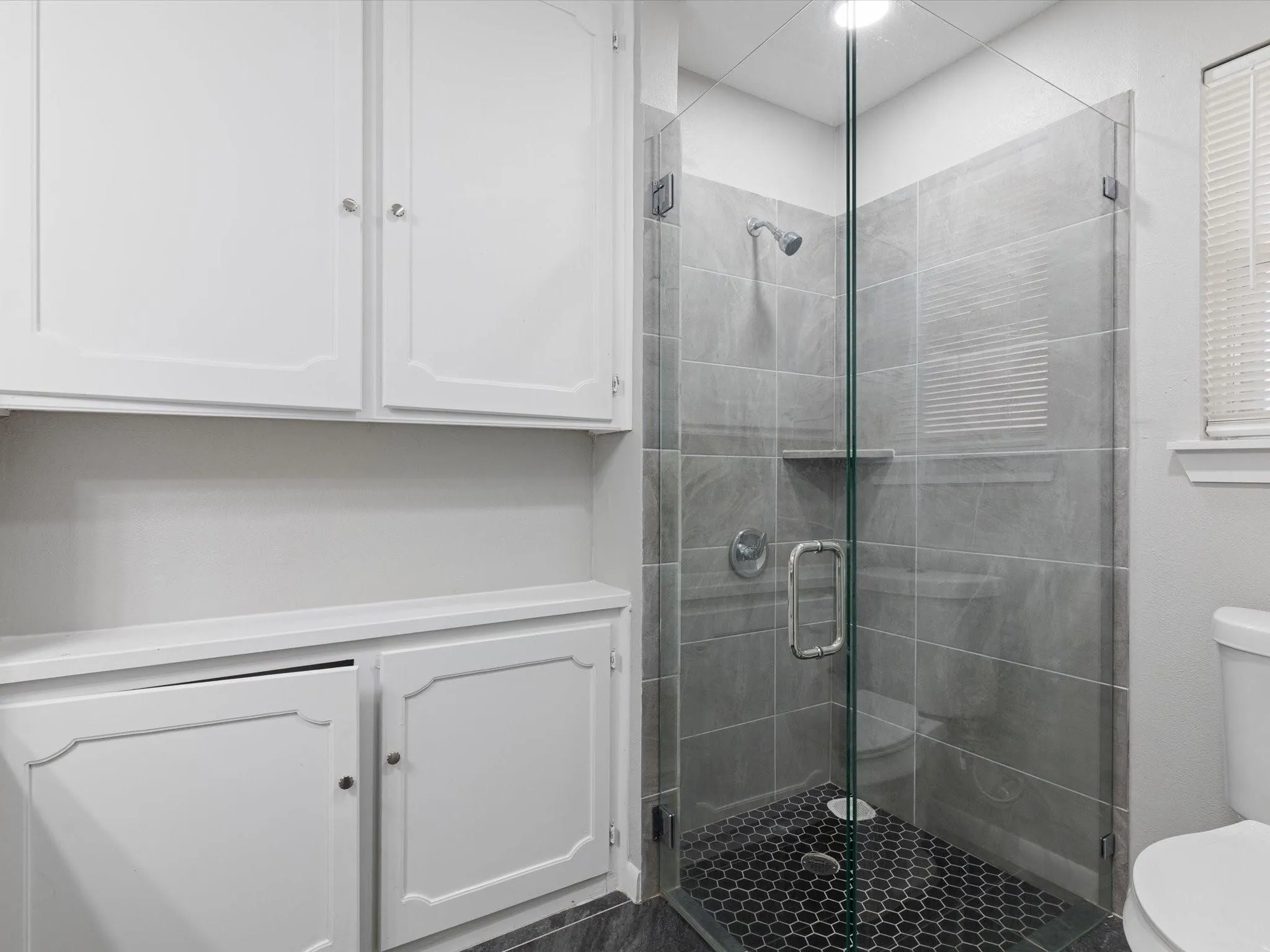 Glass-enclosed shower with gray tile surround and hex tile flooring