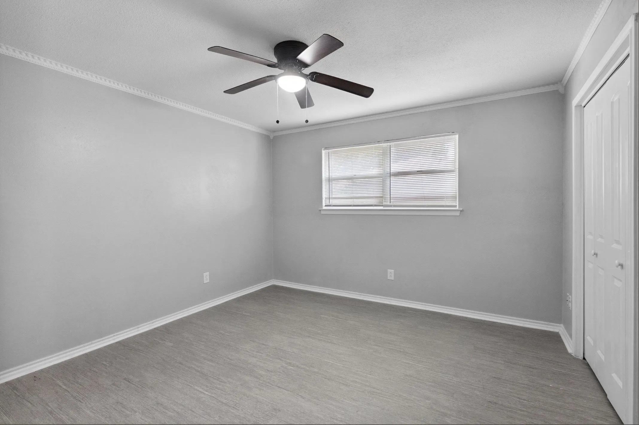 Spacious room featuring wood-finish flooring, a ceiling fan with integrated lighting, a window with blinds, and white bi-fold closet doors