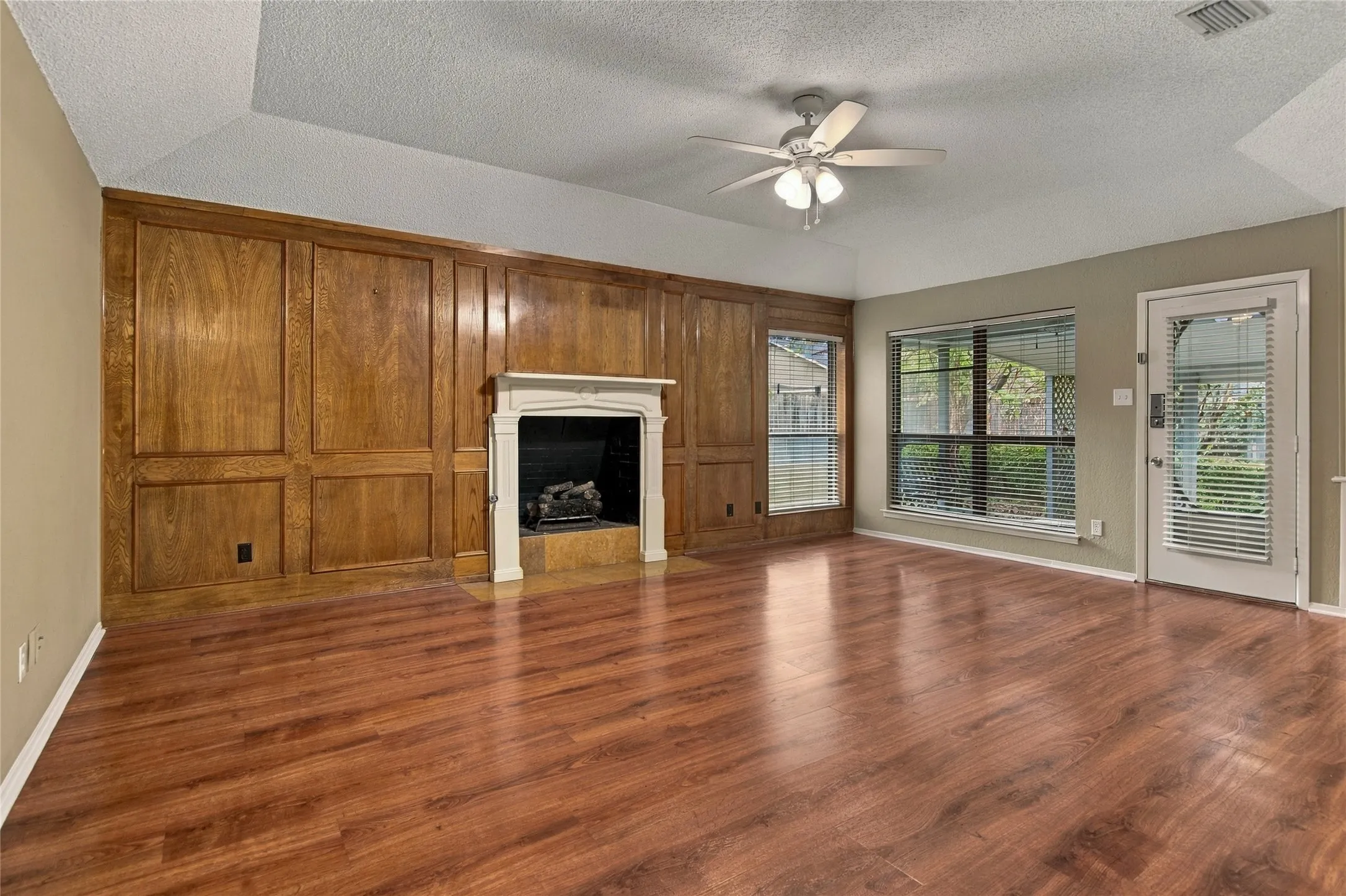 LVP flooring, wood paneling, fireplace with decorative mantel, vaulted ceiling, and ceiling fan