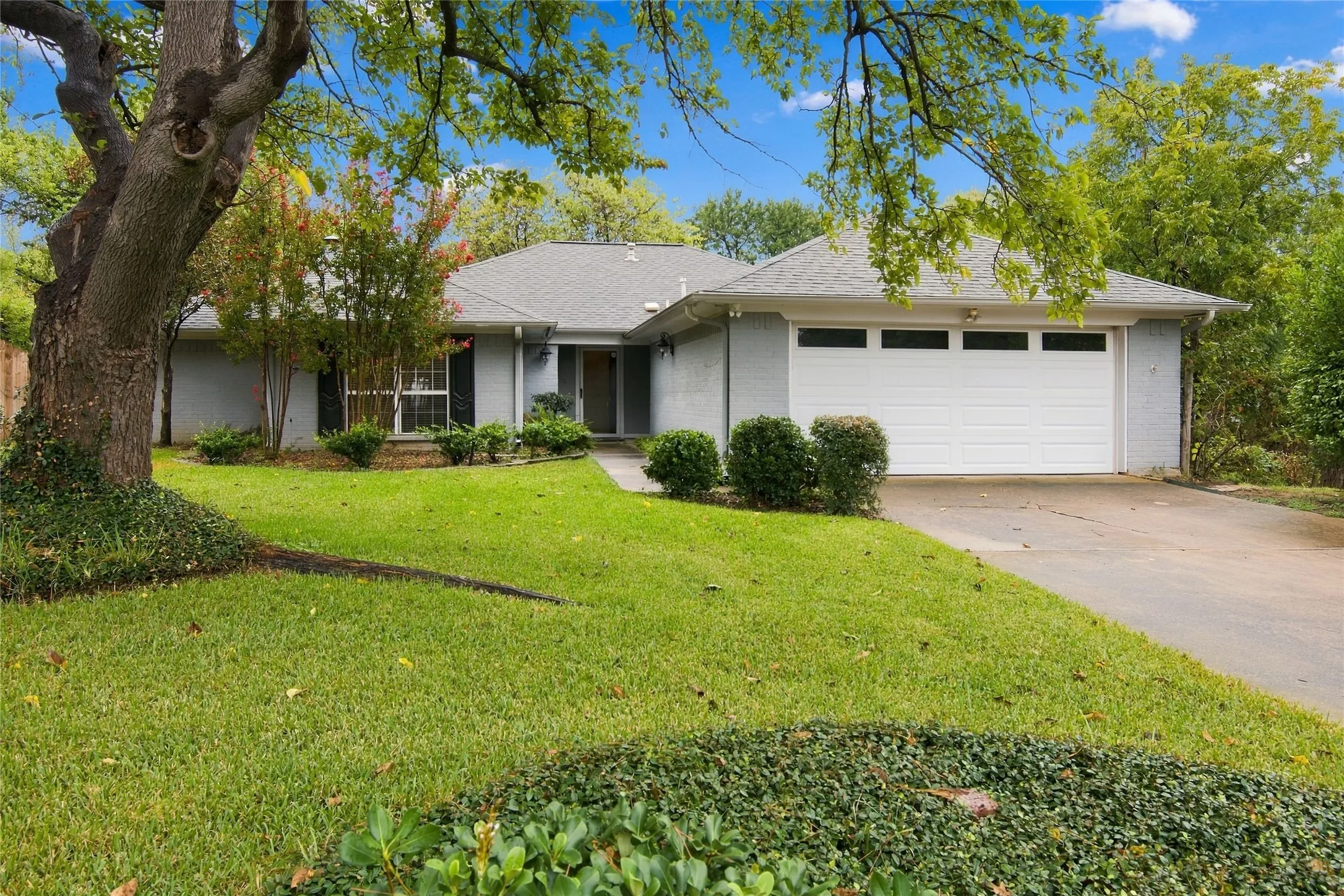 Single-story residence featuring a gray brick exterior, a white garage door with upper window, and a gray shingle roof