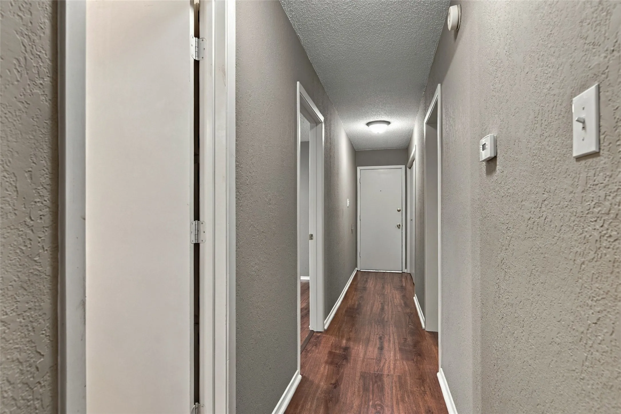 Hallway featuring LVP flooring, light grey textured walls, and a flush-mount ceiling light