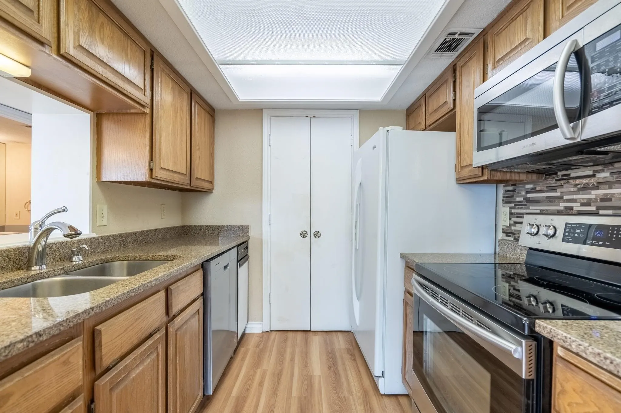 Kitchen featuring wood cabinetry, granite-style countertops, stainless steel appliances, and wood-finish flooring
