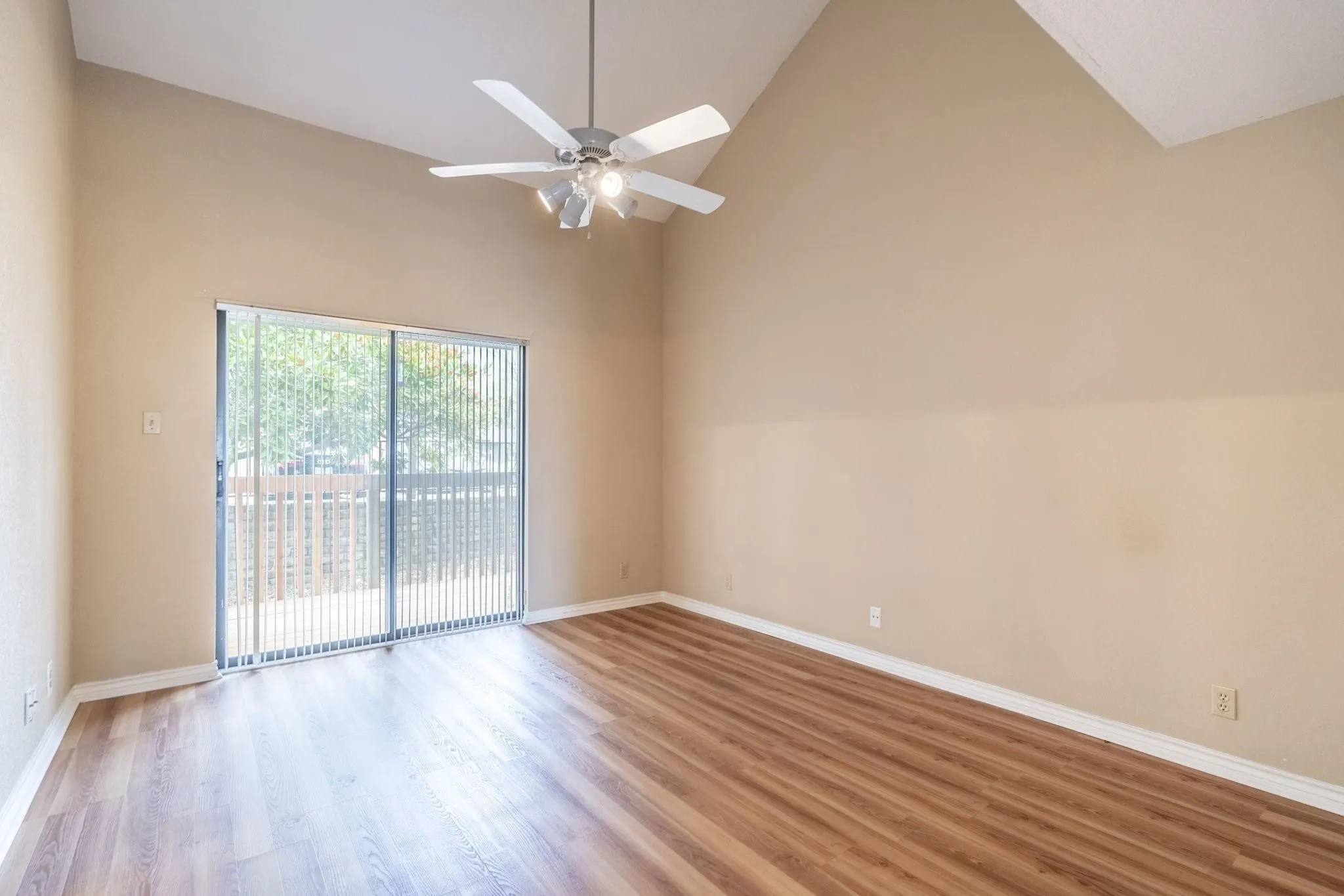 Vaulted ceiling, wood-finish flooring, ceiling fan with integrated lighting, sliding glass door, and exterior balcony