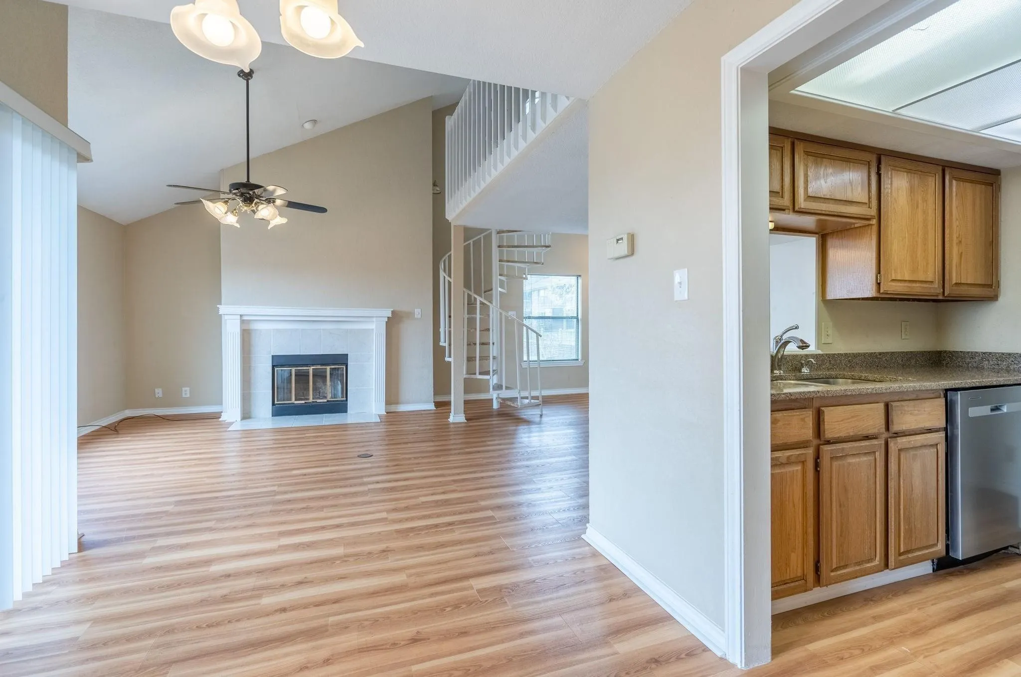 Open-concept living area with vaulted ceilings, wood-finish flooring, a fireplace with a mantel, and a spiral staircase