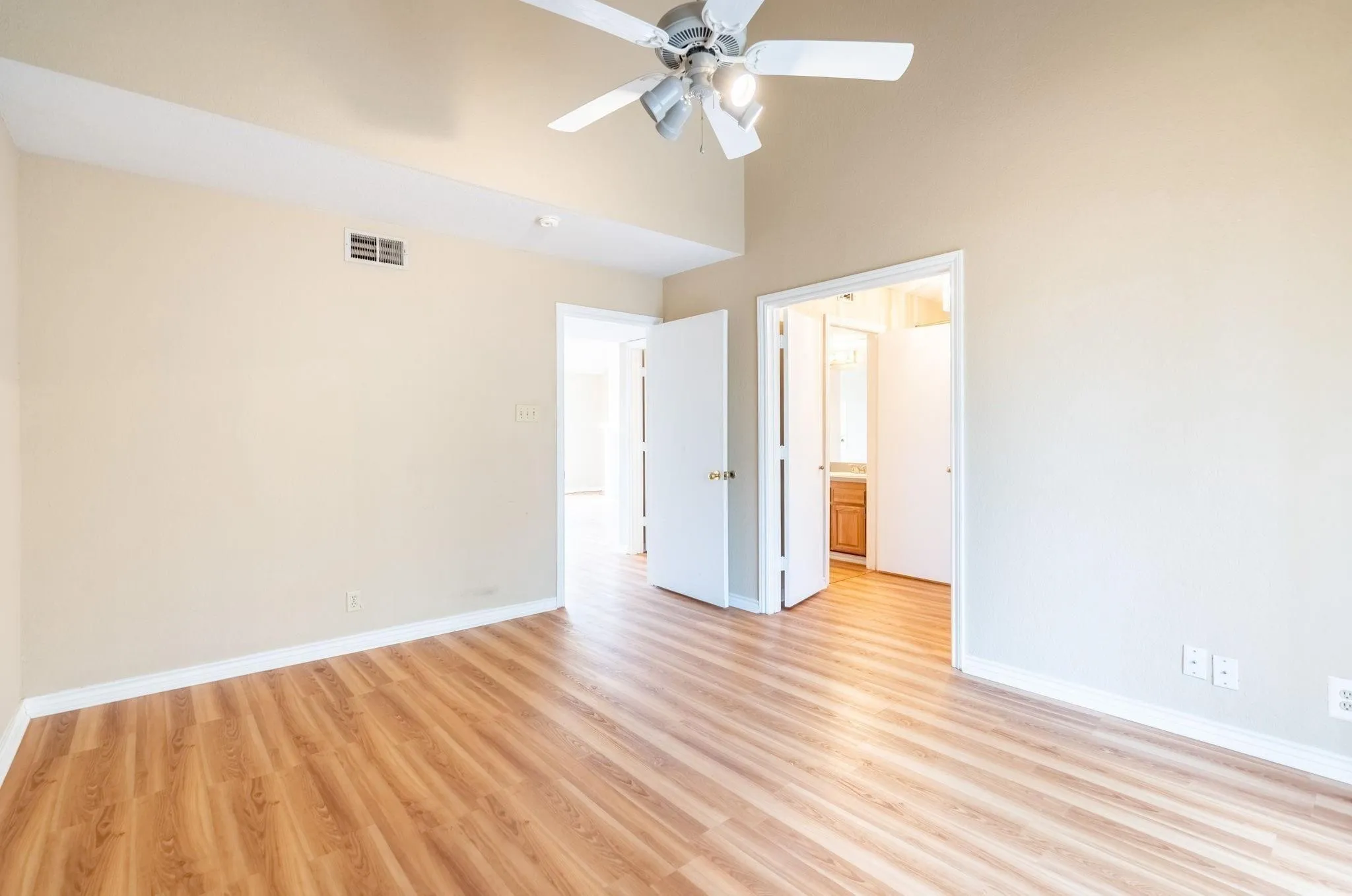 Vaulted ceiling with a ceiling fan light fixture, wood-finish flooring, and white trim