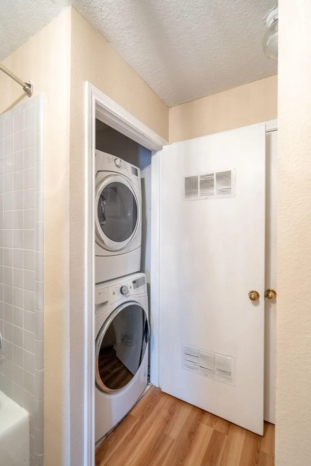 Stackable laundry appliances, wood-finish flooring, white tiled shower surround