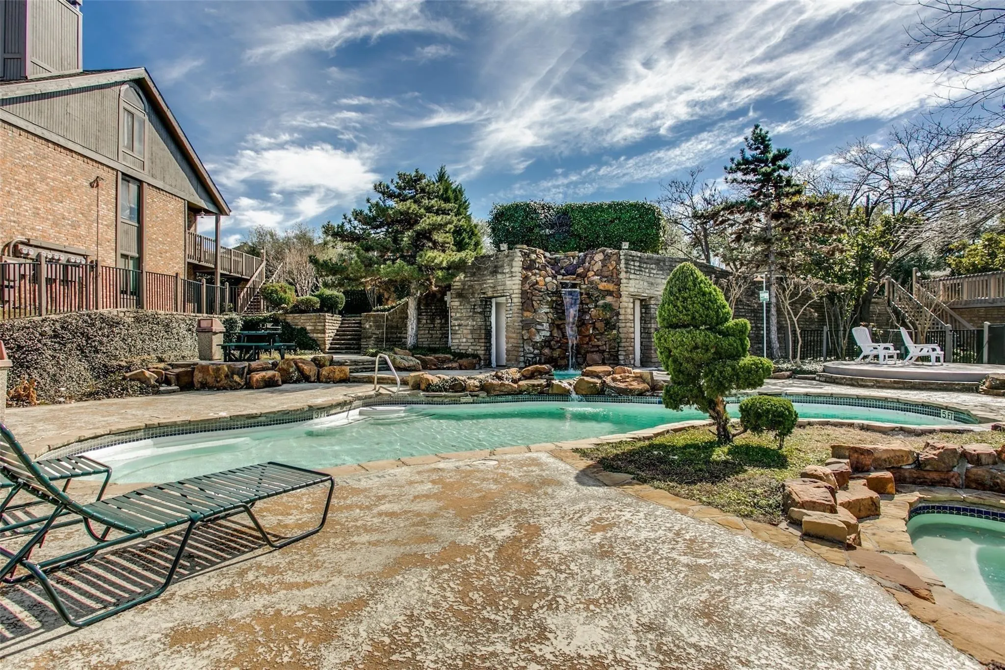 Multi-level swimming pool with a rock waterfall feature, stone deck, and separate hot tub