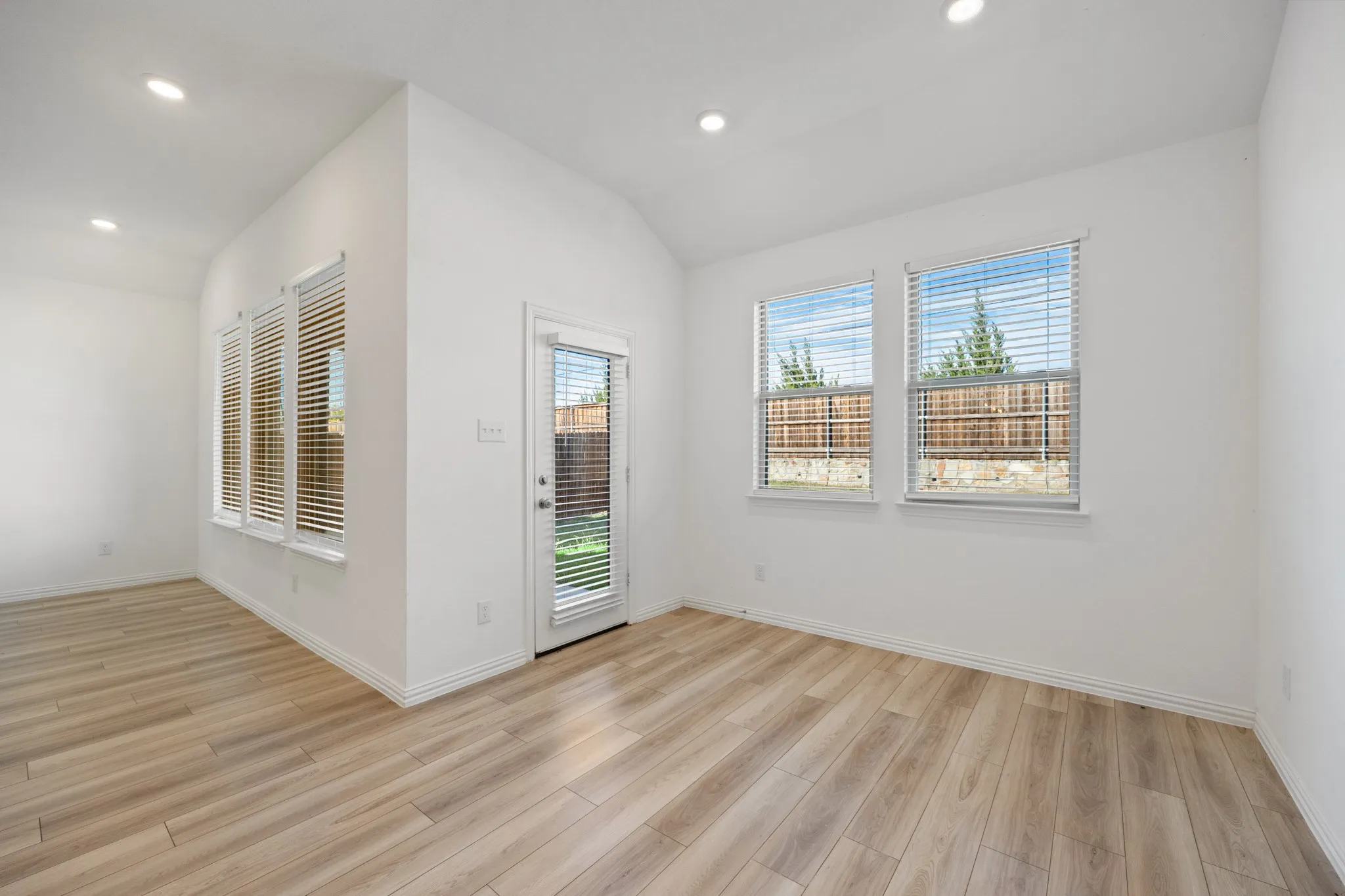Vaulted ceiling with recessed lighting, wood-finish flooring, multiple windows, and a glass-paneled door