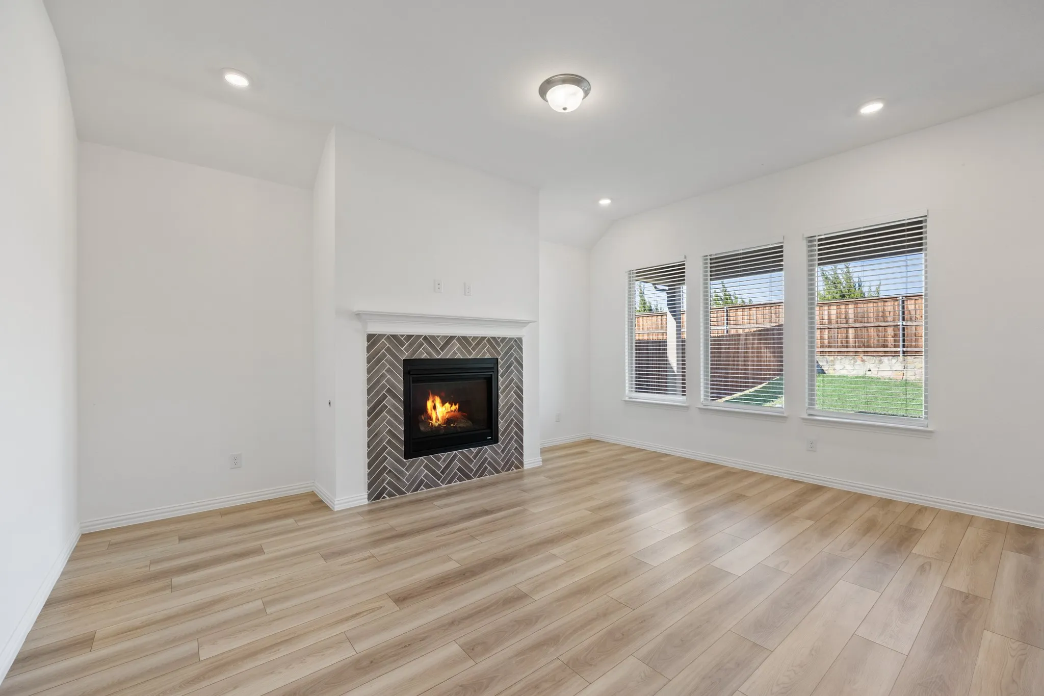 Vaulted ceilings, recessed lighting, wood-finish flooring, three large windows, and a fireplace with a herringbone tile surround