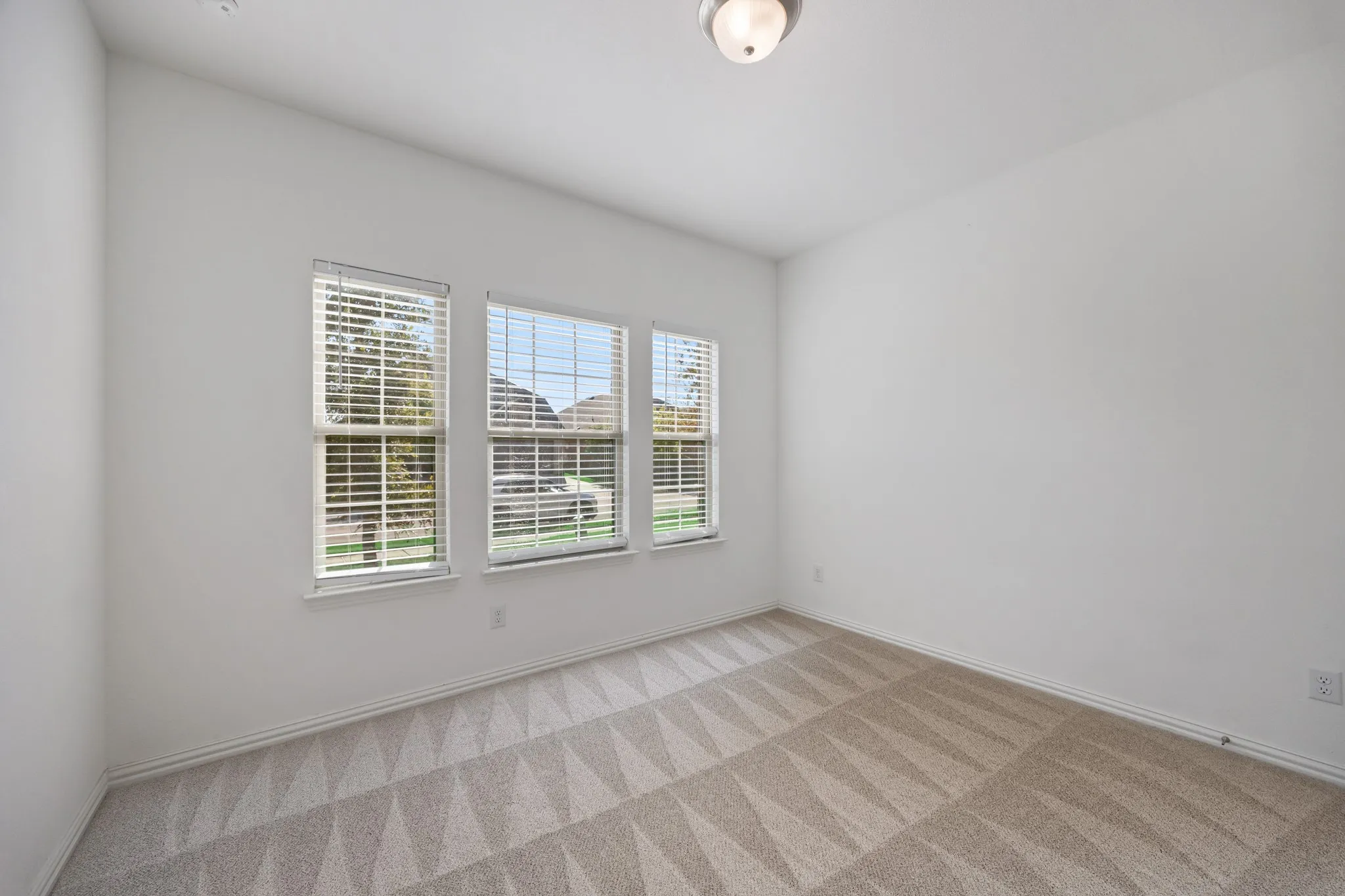 Three windows with blinds, patterned carpeting, white walls, and a ceiling-mounted light fixture