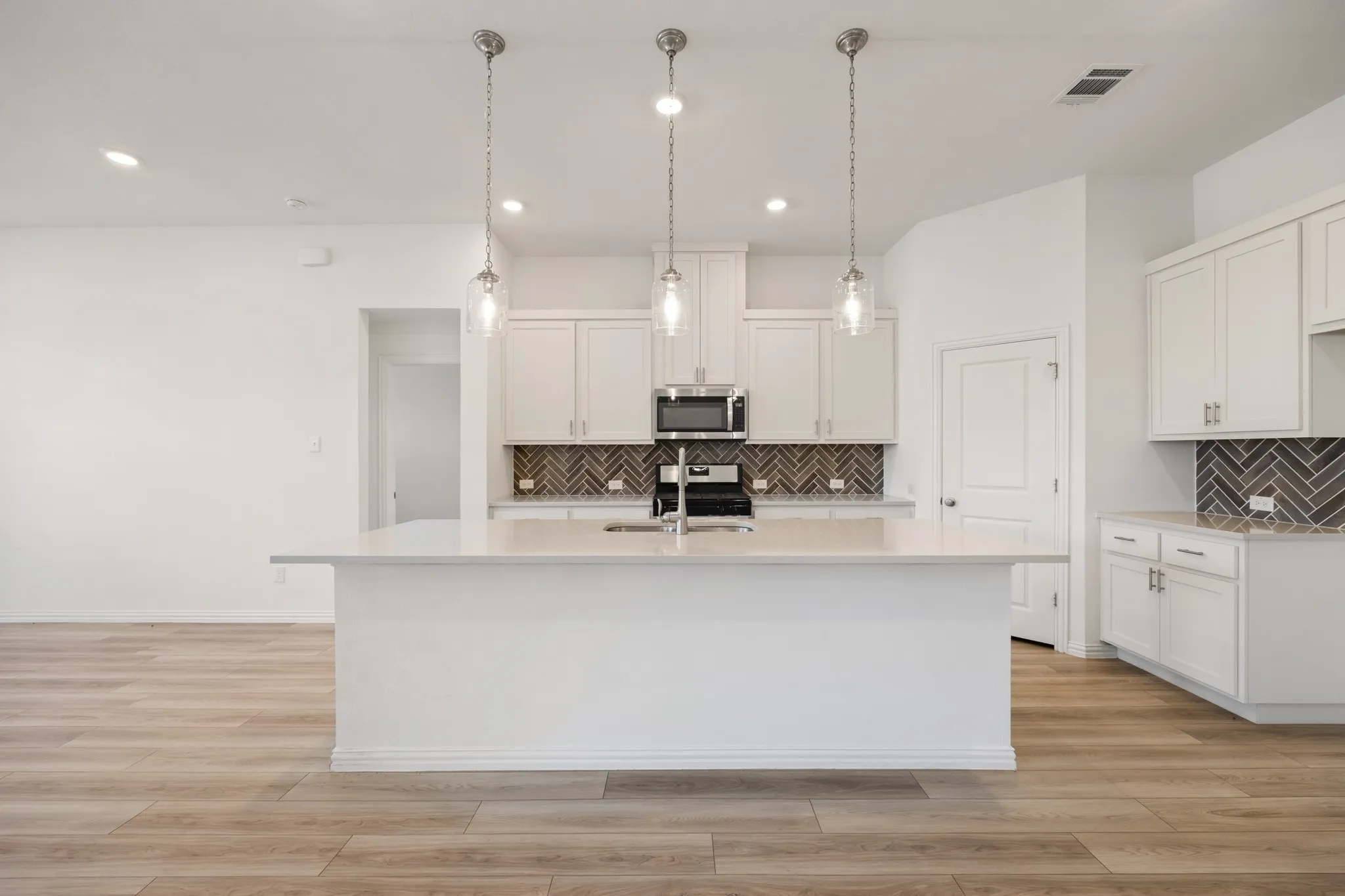 Kitchen featuring an island with countertop seating, white cabinetry, a herringbone tile backsplash, and stainless steel appliances