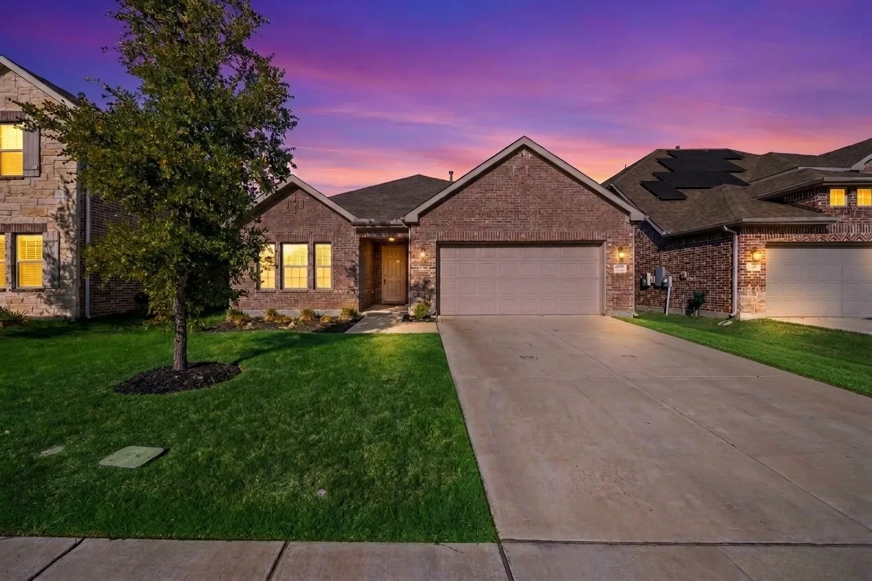 Brick exterior, attached two-car garage, concrete driveway, front lawn with a single tree, and exterior lighting fixtures