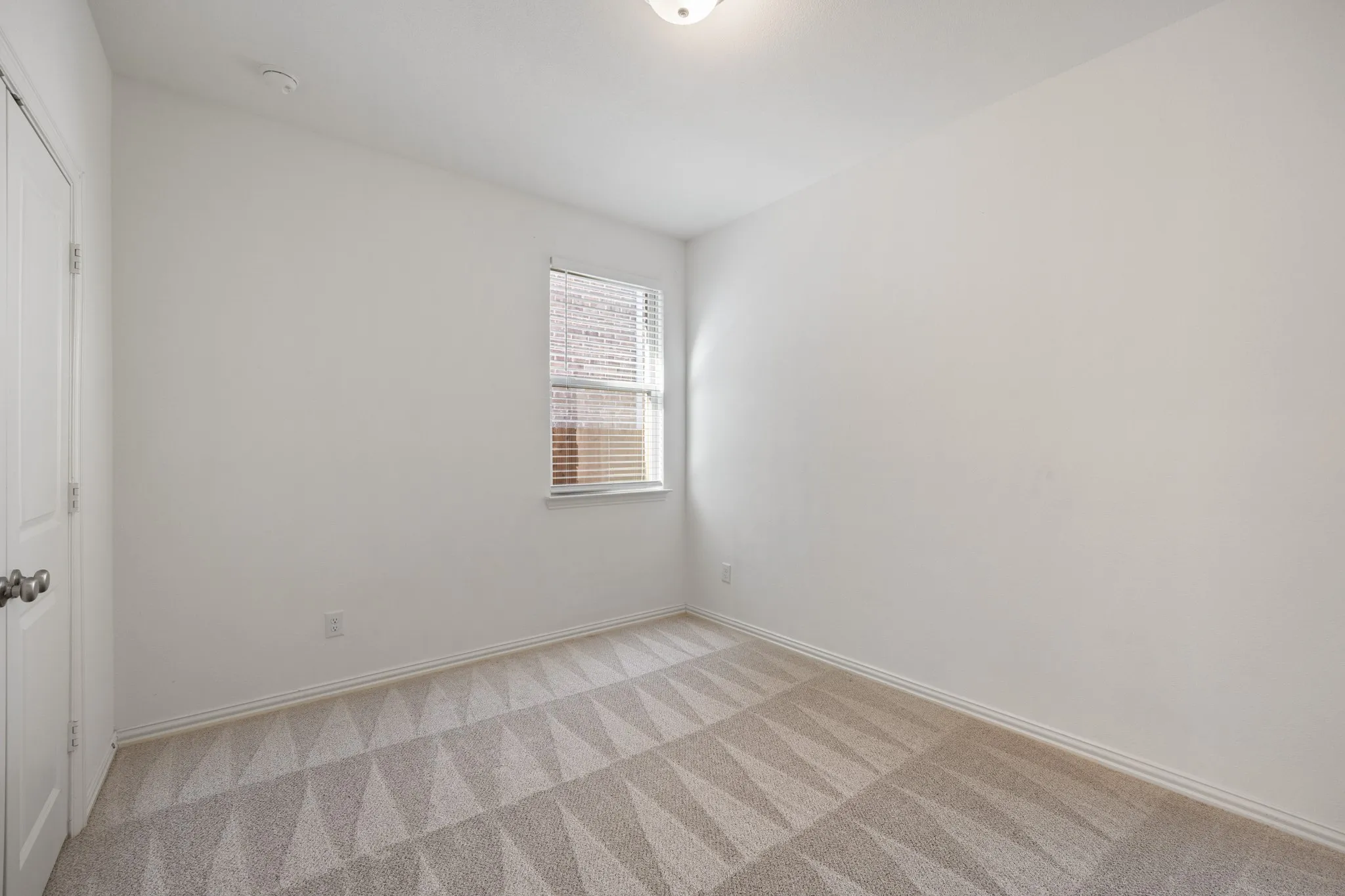 White walls with patterned carpeting and a single window with blinds