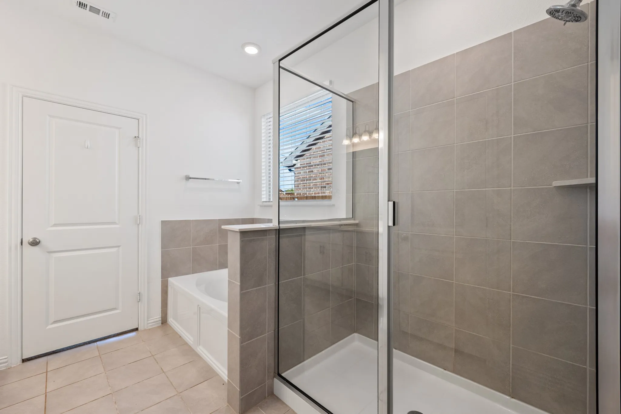 Recessed lighting illuminates a tiled shower with a glass enclosure, an integrated shower bench, and a built-in bathtub with a tiled surround